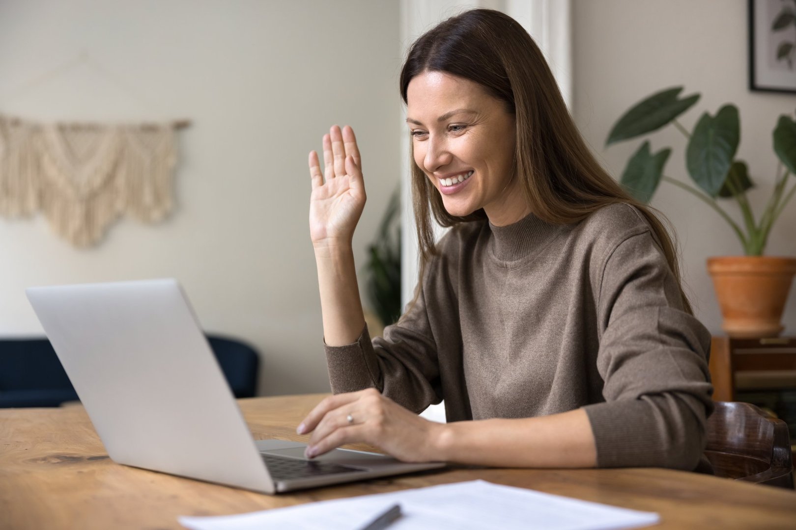 Smiling woman working remotely, start on-line consultation using videocall application on modern laptop. Happy female make virtual meeting event, greet colleague seated at workplace desk with computer