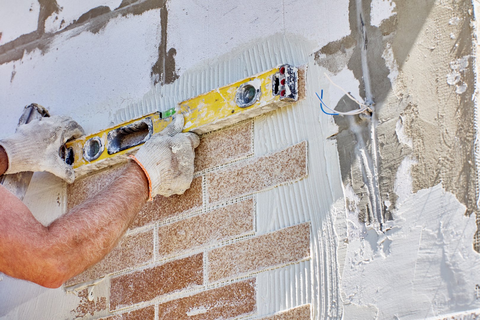 House painter uses spirit level to ensure faux brick panel is accurately positioned relative to horizontal plane.