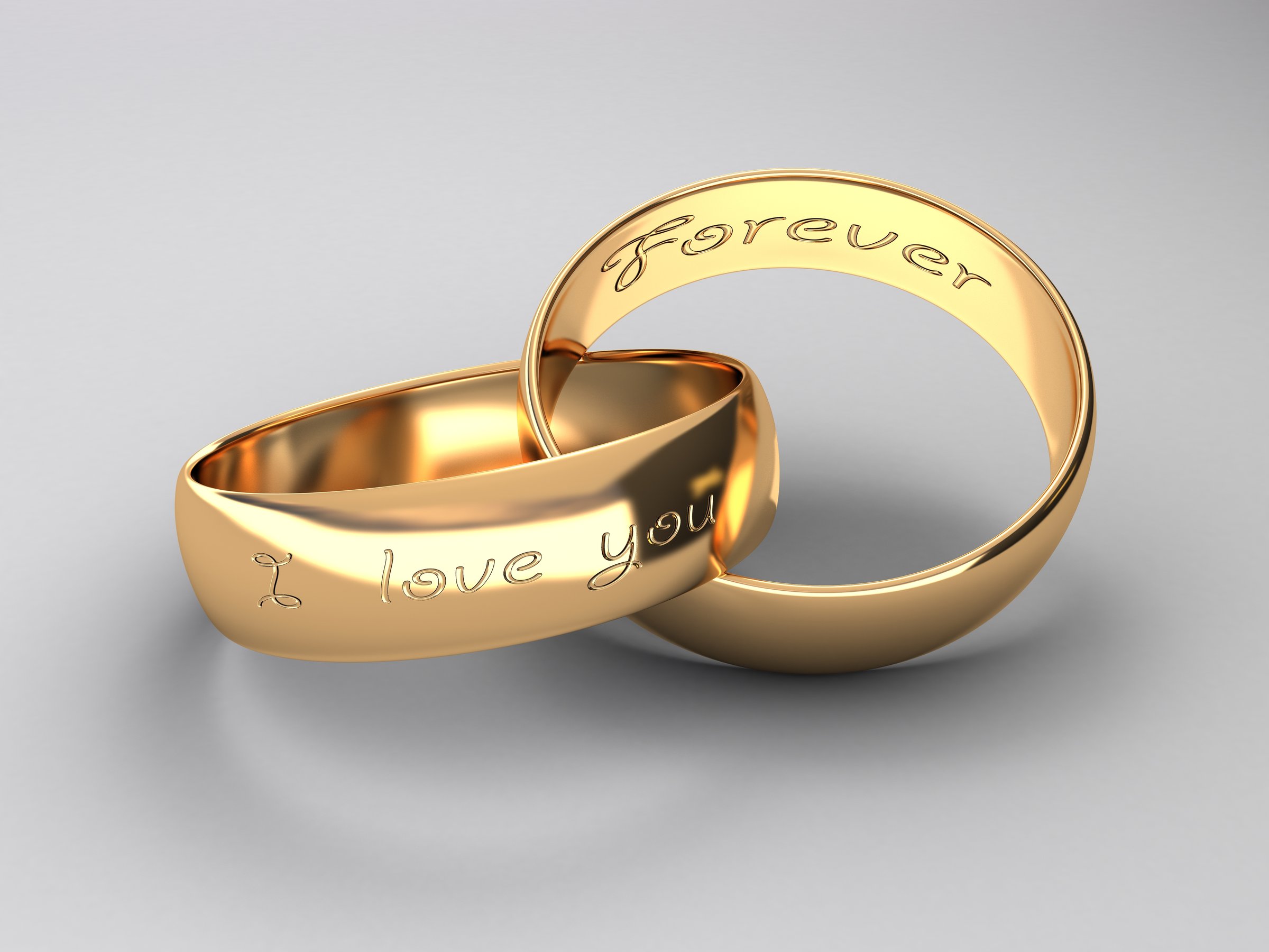 Two gold rings with engravings Forever and I love you against a plain background.