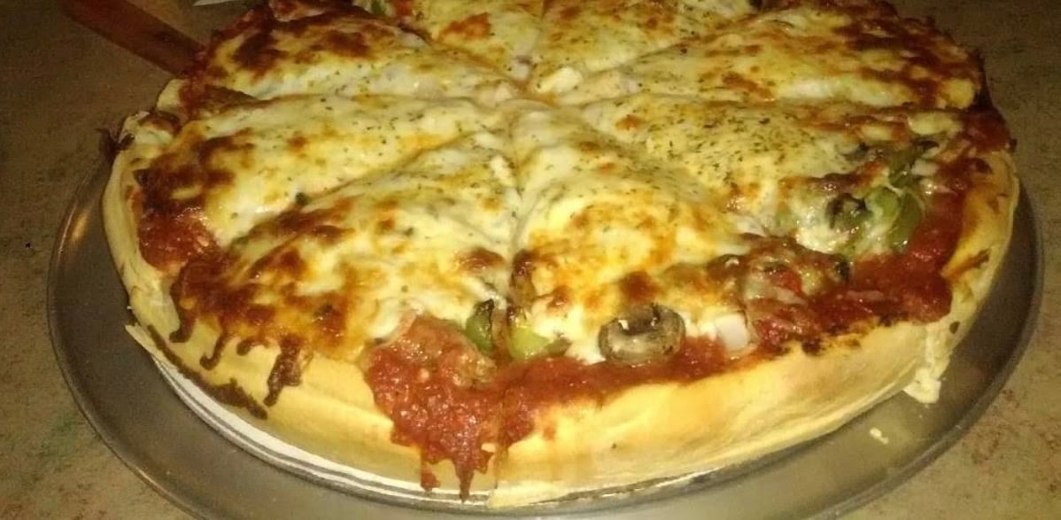 Freshly baked pizza with melted cheese, toppings, and herbs on a round tray, sliced into six pieces.