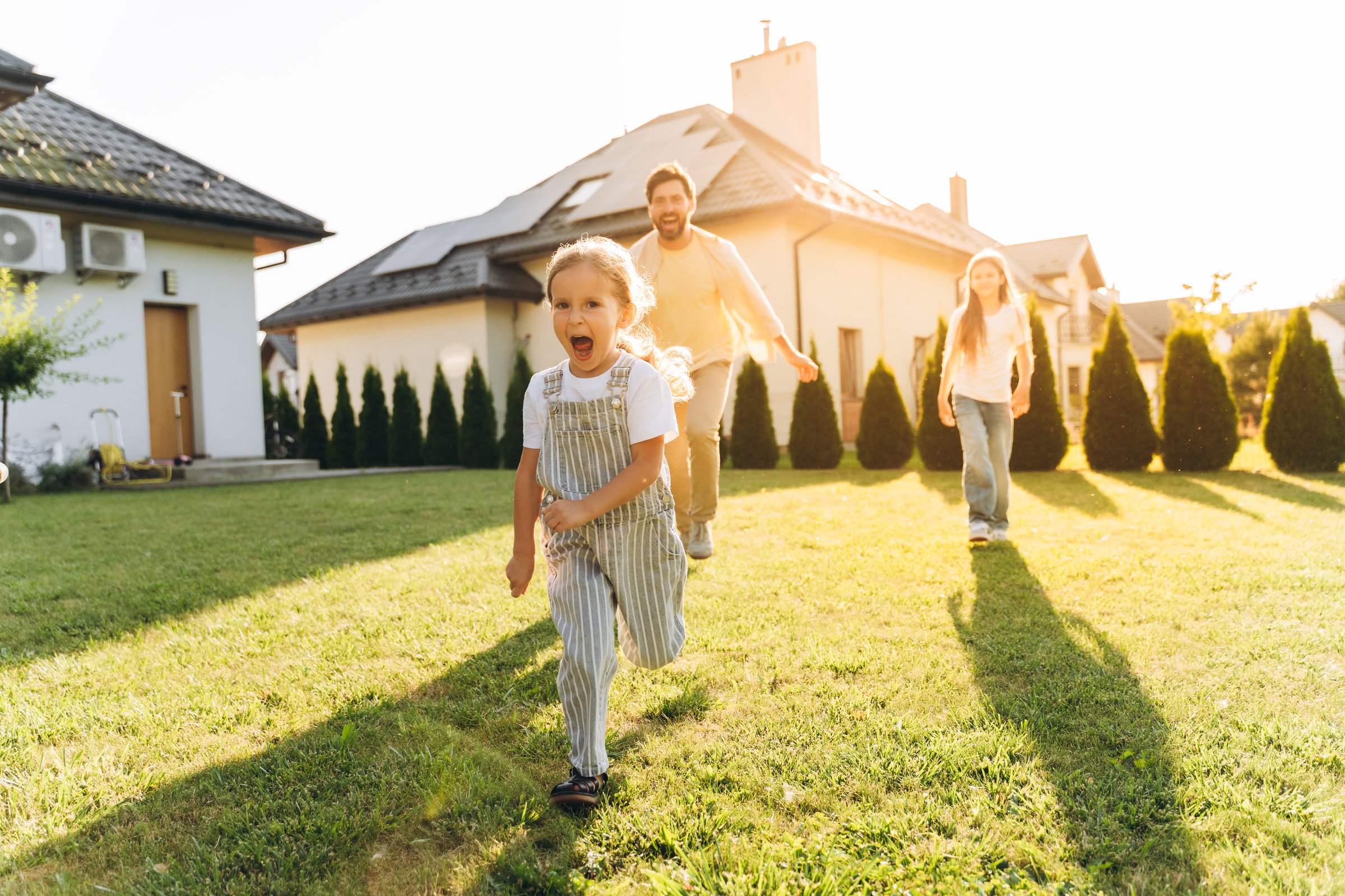 Happy family enjoying time together, playing and running joyfully in the sunny backyard of their home on a warm summer day
