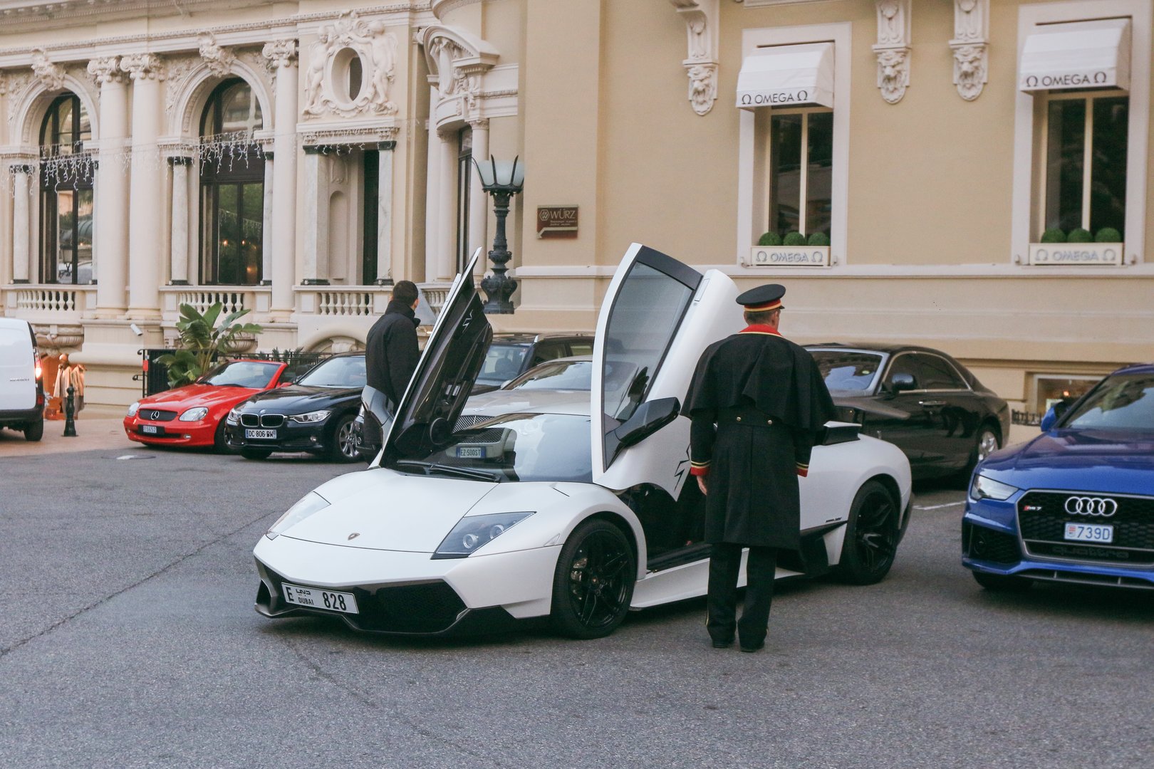 Monaco, Monaco - January 11, 2025: A sleek white luxury car with open doors is parked outside Casino de Monte Carlo while a guard oversees the area.