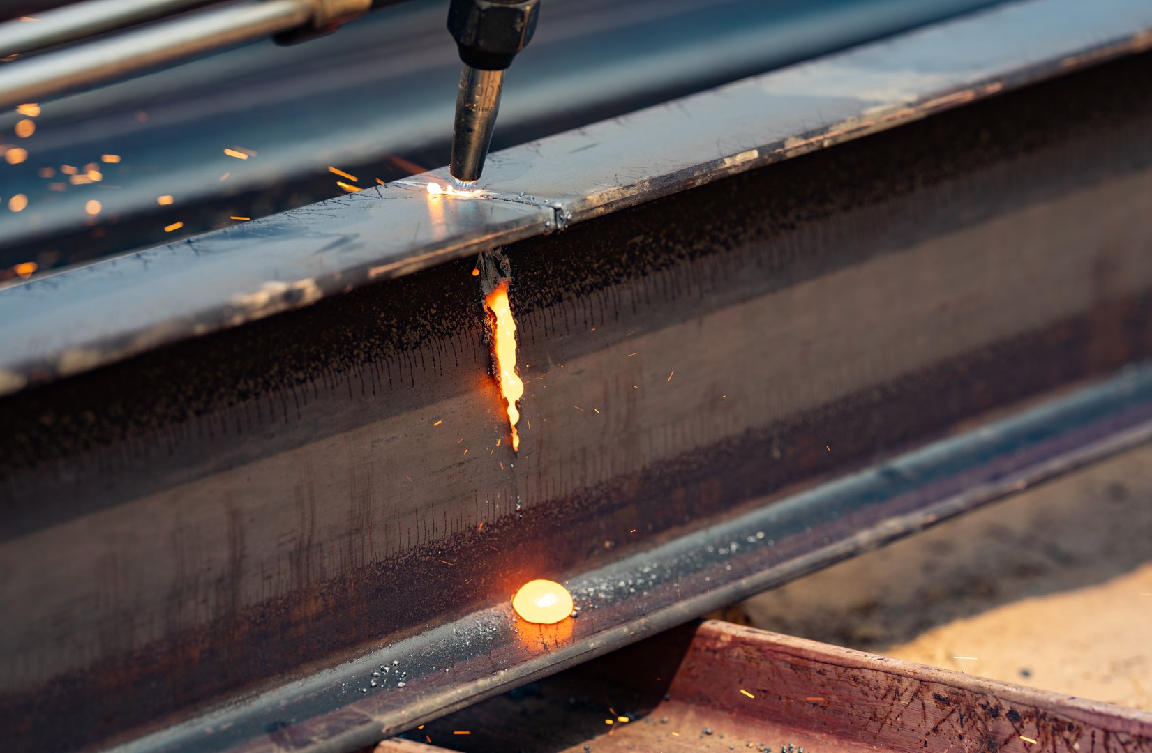Welder working on metal beam, emitting bright sparks as part of welding process. Skilled labor. Danger of industrial work, and craftsmanship required in metal fabrication. Skilled hands control flame.