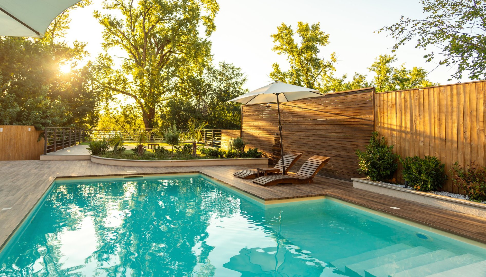 Swimming pool in modern private villa with lounge chairs, palm trees and umbrella at sunset