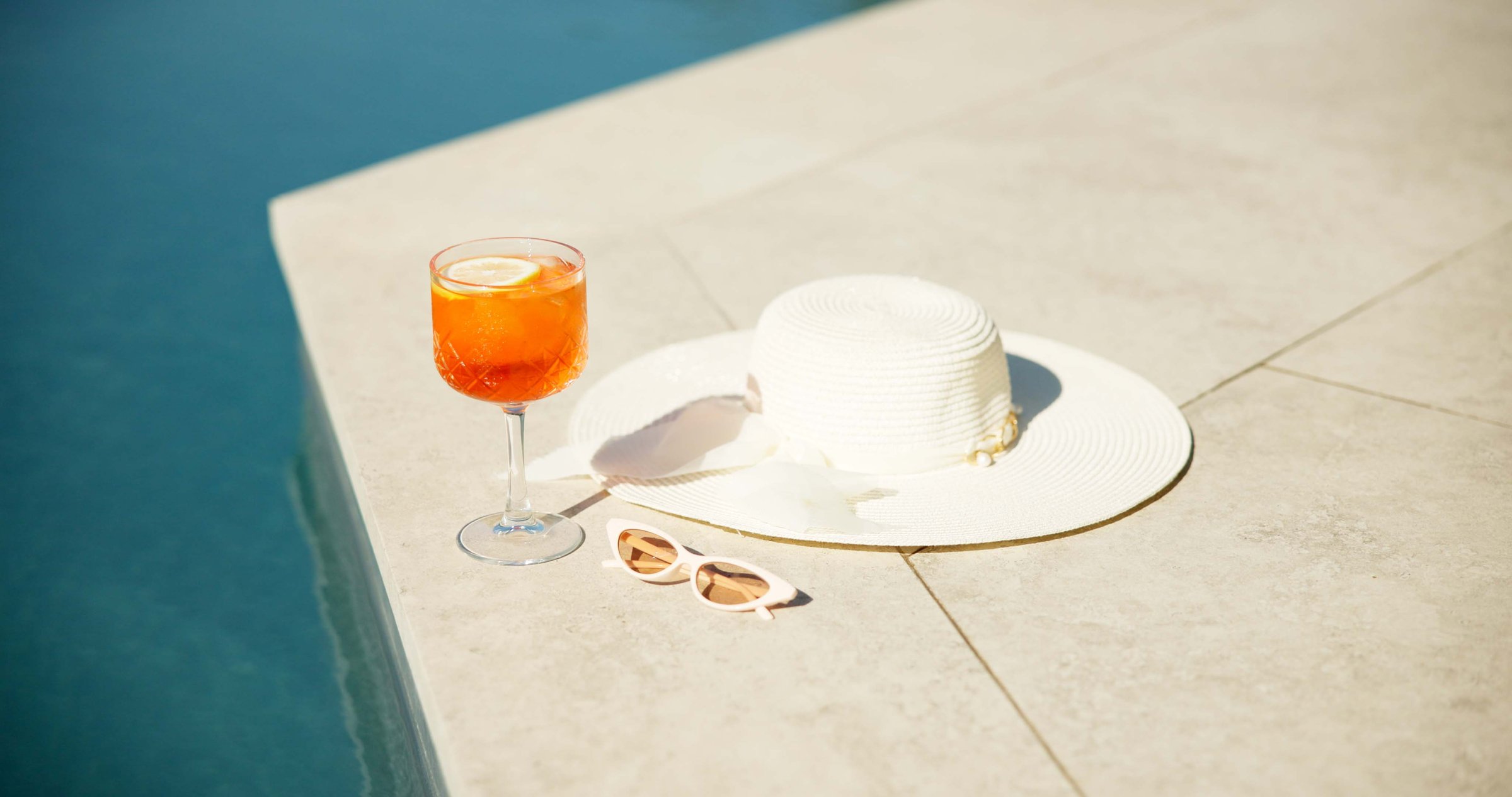 Cocktail, alcohol and swimming pool with sunglasses and hat for summer holiday or vacation. Travel, resort and drink by water for outdoor luxury, hotel hospitality and break to relax or chill