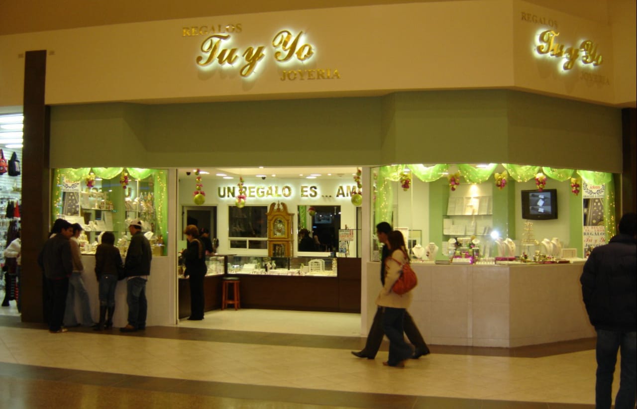 Jewelry store with green decor and people browsing the display cases inside a shopping mall.
