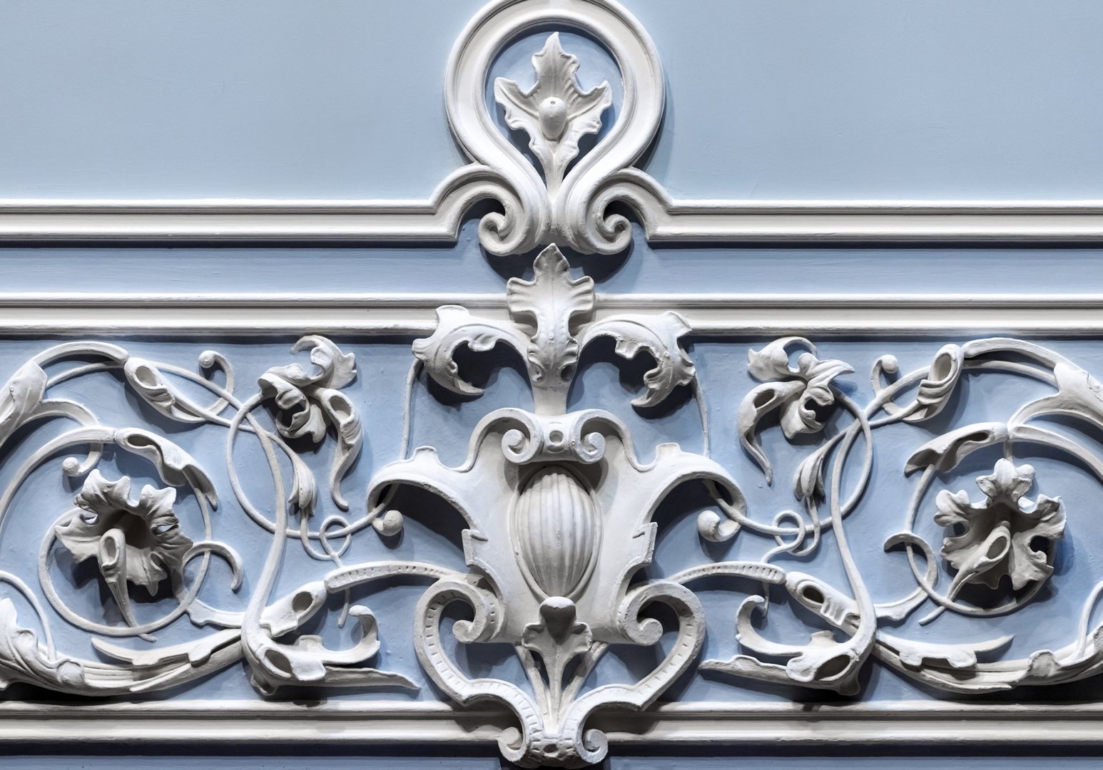 Beautiful ornate decorative plaster moldings showcasing intricate patterns, curves, and floral motifs against a soft blue wall background, exemplifying classic elegance and detailed craftsmanship