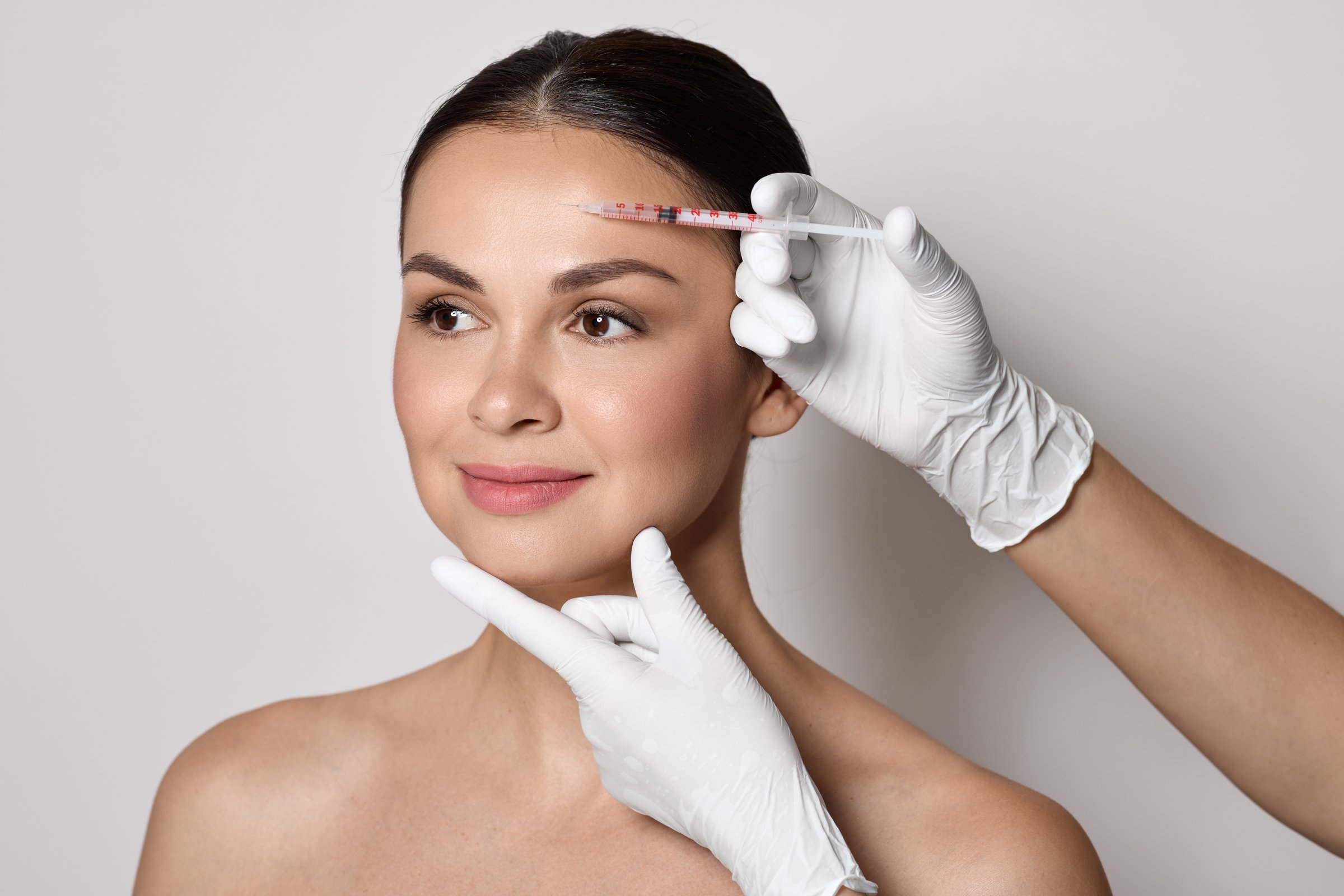 Botulinum toxin injections near a woman's forehead for blocking mimic wrinkles and wrinkles removal. Beautiful female face, close-up on grey background