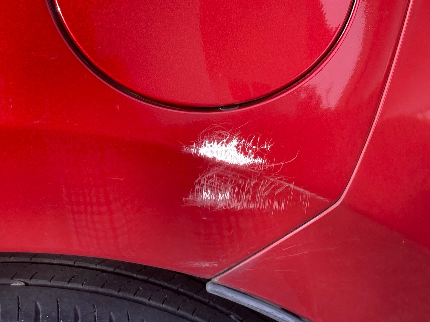 A little scratch at the left side of a red car, a position is between a rare wheel and a gas tank.