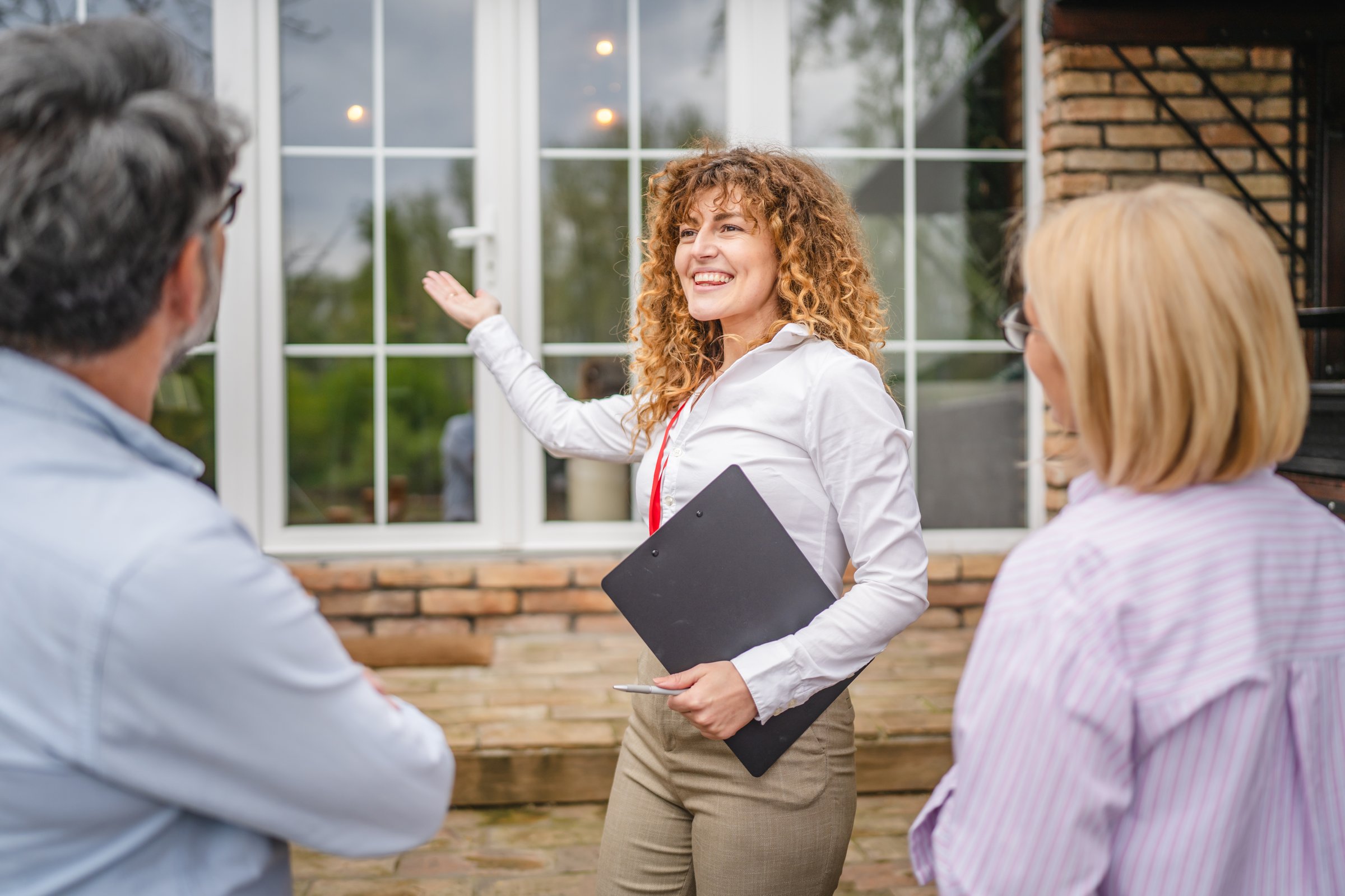 under the shoulder view of beautiful woman real estate agent present house to mature couple