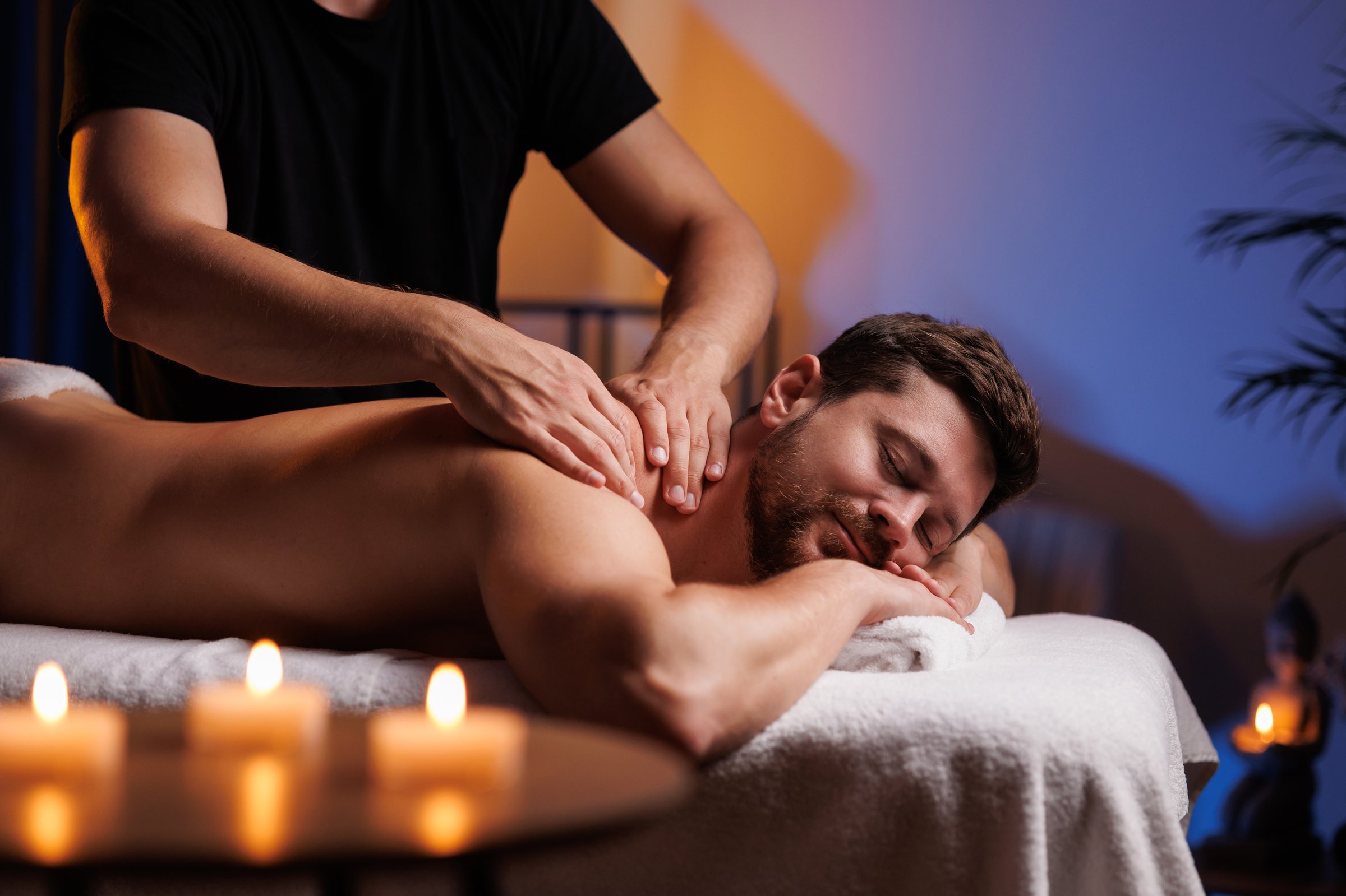 Male masseur massaging the back and shoulders of a man lying on a massage table in a relaxing atmosphere in a spa salon. Therapeutic restorative body massage after office work, health concept