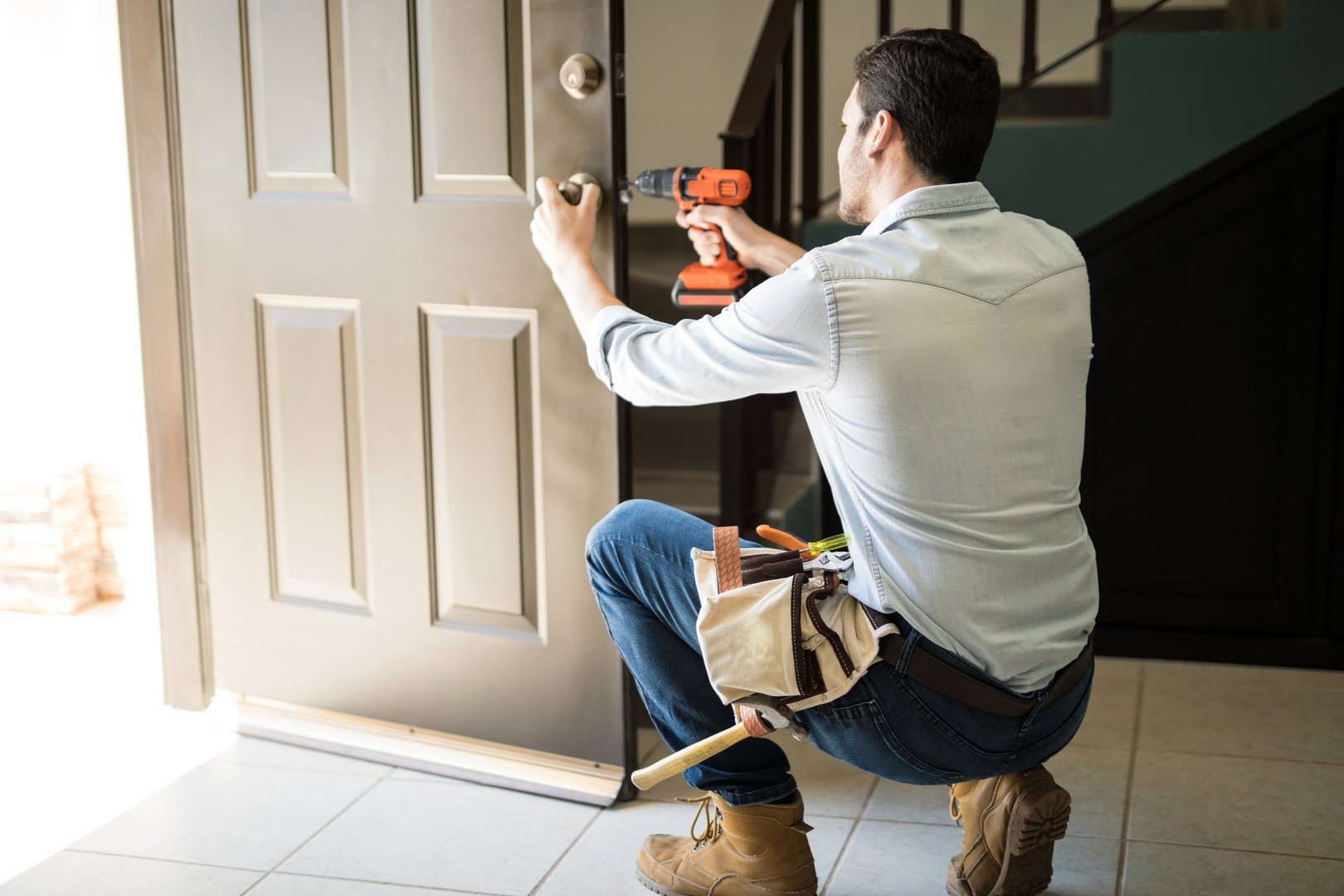 Rear view of a good looking man working as handyman and fixing a door lock in a house entrance