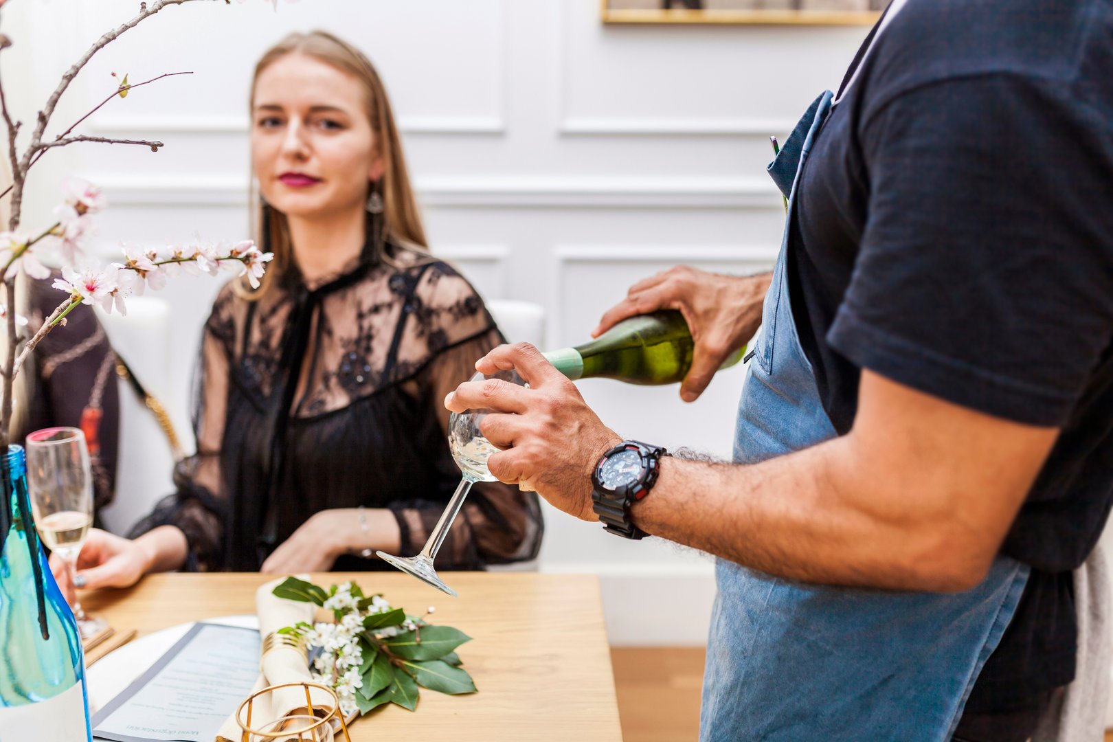 Latin american male cook serving wine to clients during stylish private dinner with a group of people at home. Alcohol, beverage, drink concept.