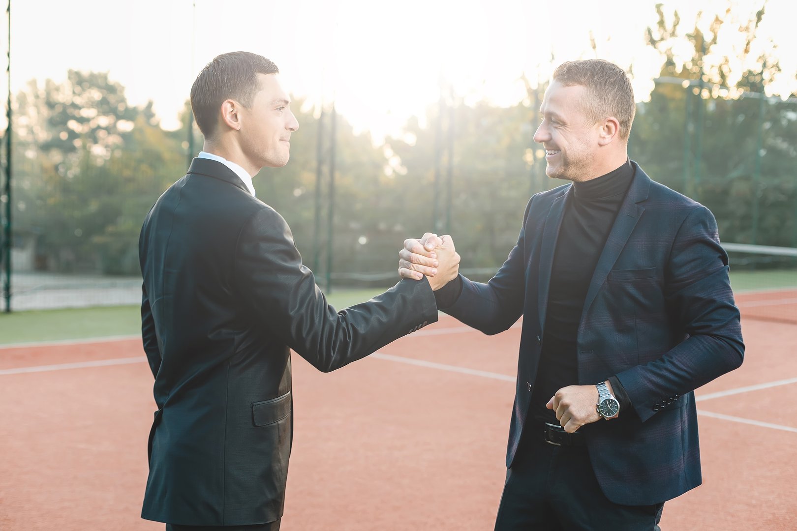 Business handshake. Two confident business men shaking hands while standing outdoors. Two men shaking hands during a meeting on tennis court background, success, dealing, greeting and partner.
