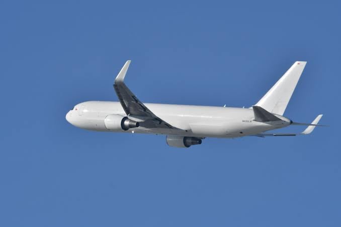 A white commercial airplane flying against a clear blue sky, showing its left side and tail.