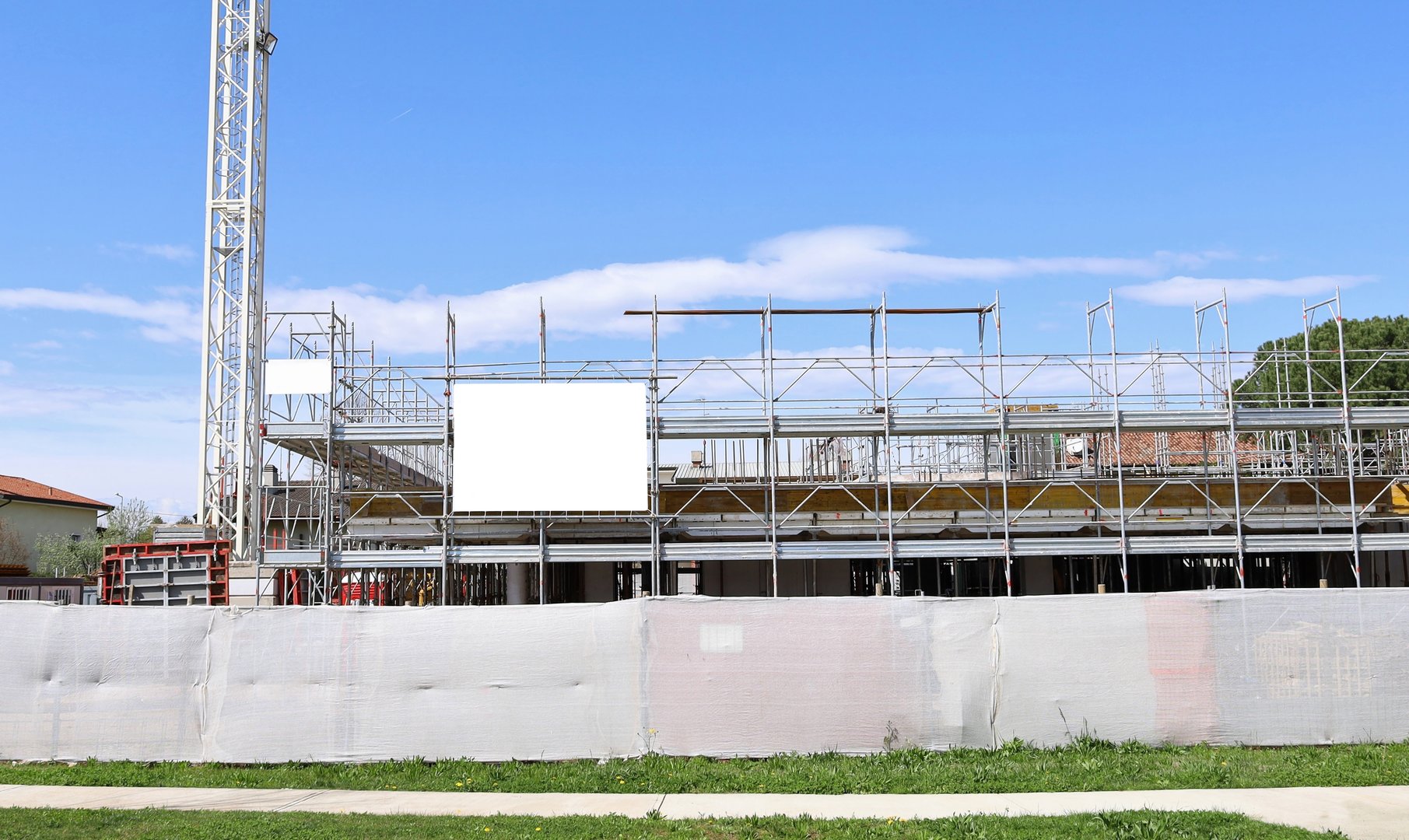 White plastic fence surrounding  the construction site and a blank information board on the scaffolds covering the residential building.  Background for copy space.