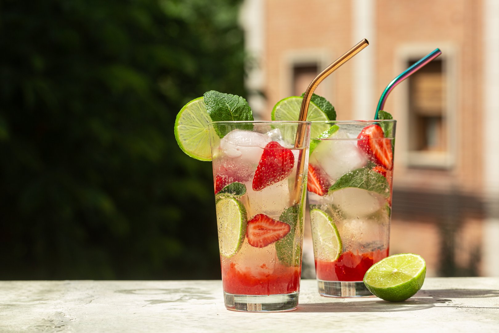 Refreshing summer cocktail with strawberries, lime, mint leaves, ice cubes. Strawberry mojito. Cold fresh drink  in a glass, green outdoor  on background, hard light.