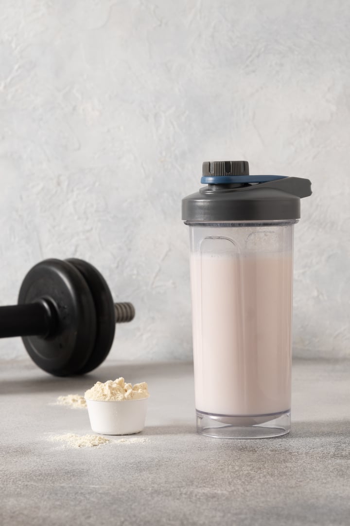 Whey protein shake and dumbbell on gray background. Close up.