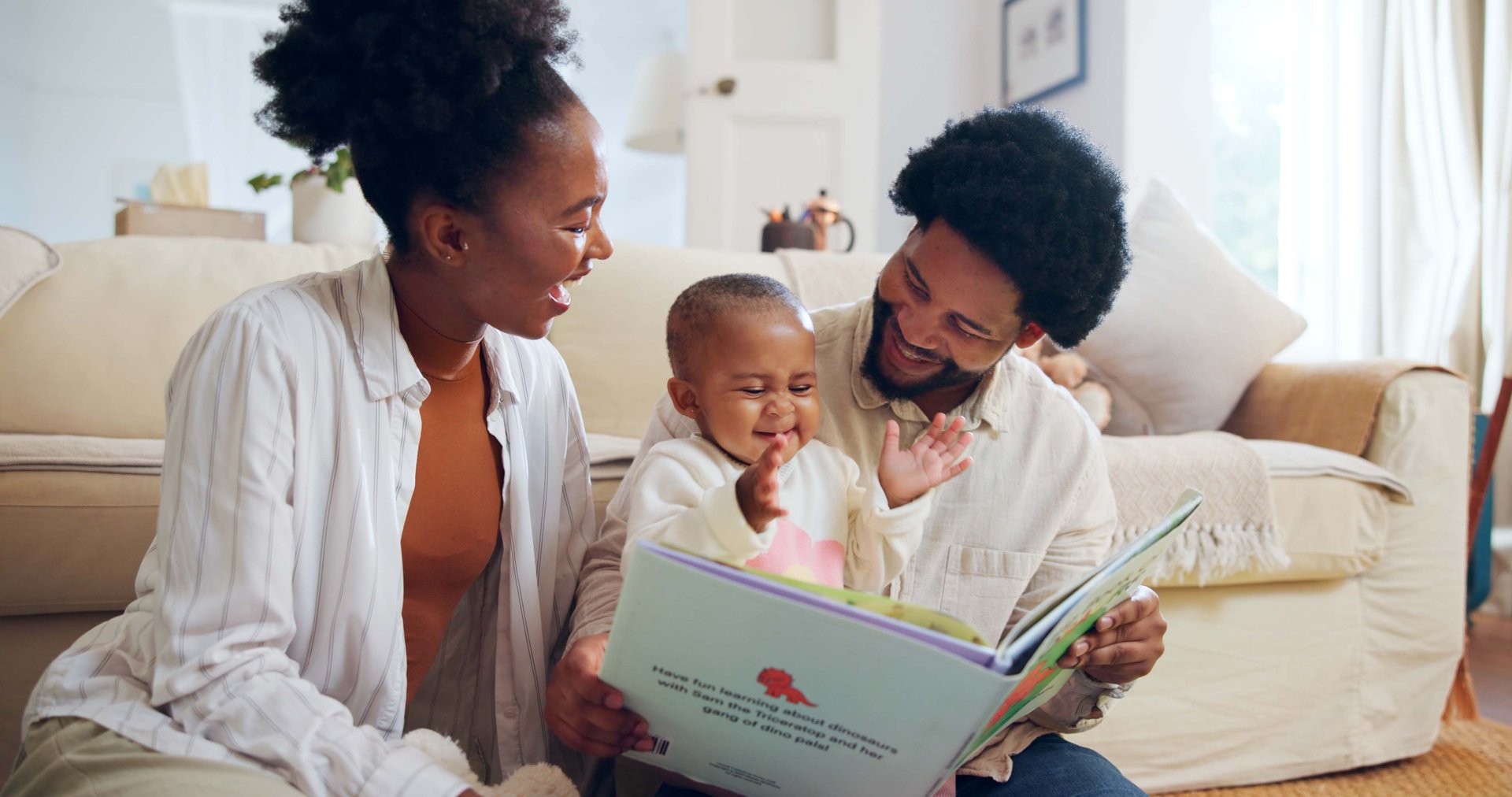 Happy, black family and reading book with child in home for story, bonding or childhood development. Mom, dad and toddler with kids novel, dinosaur or smile for learning or fantasy together in house