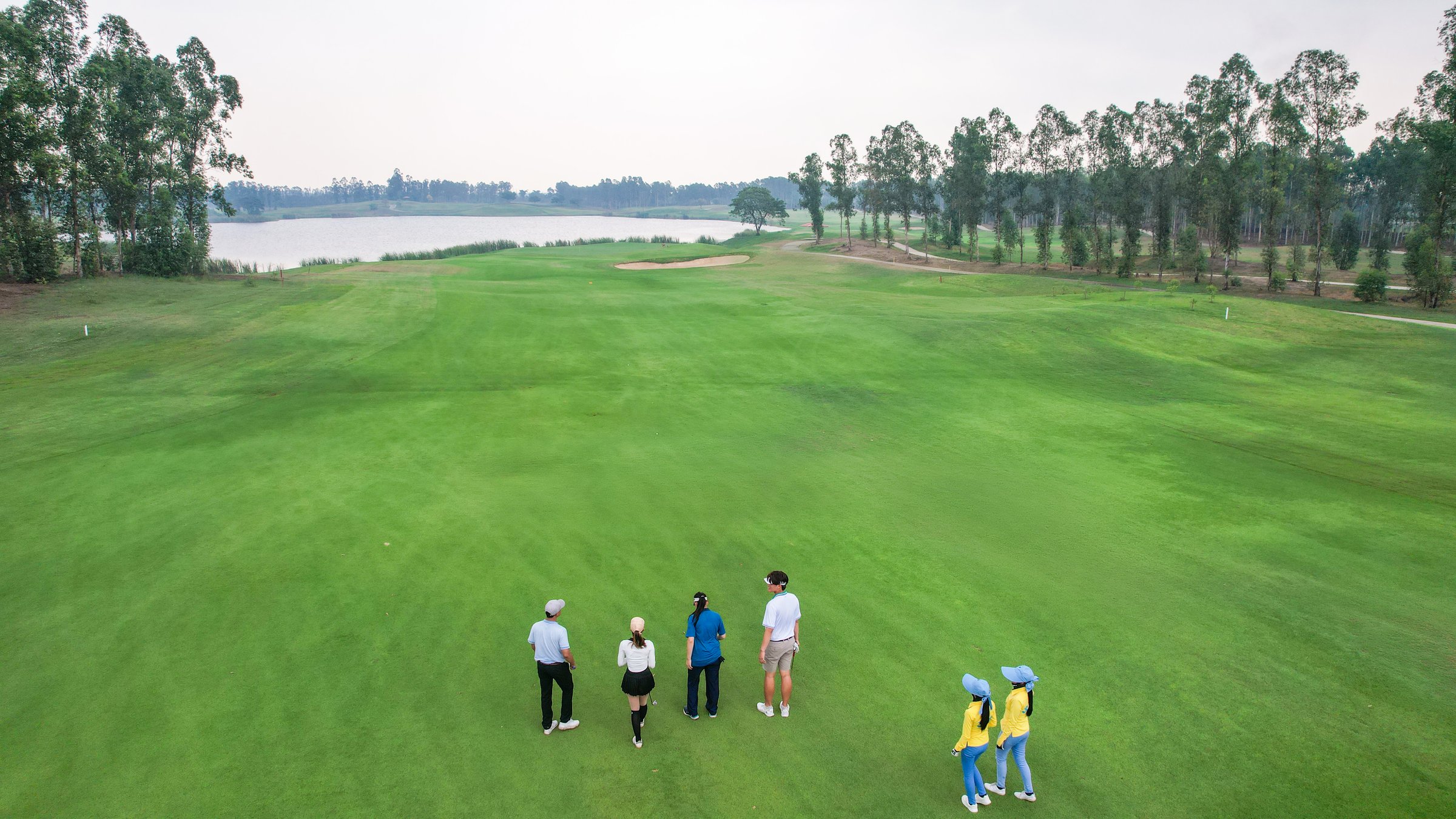 Drone view group of young pro golfers walk across lush green fairway. Attractive athletes enjoy outdoor recreation with light exercise and sport lifestyle while playing golf at course ground together