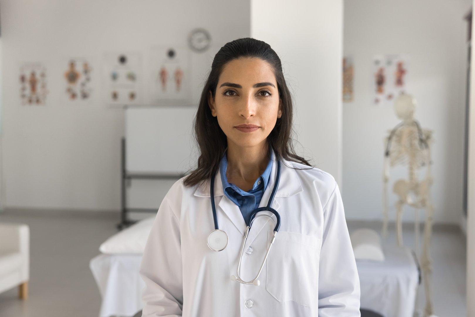 Serious medical intern girl posing in clinic educational boardroom, looking at camera, promoting career in medicine, healthcare examination. Young Latin doctor woman professional portrait