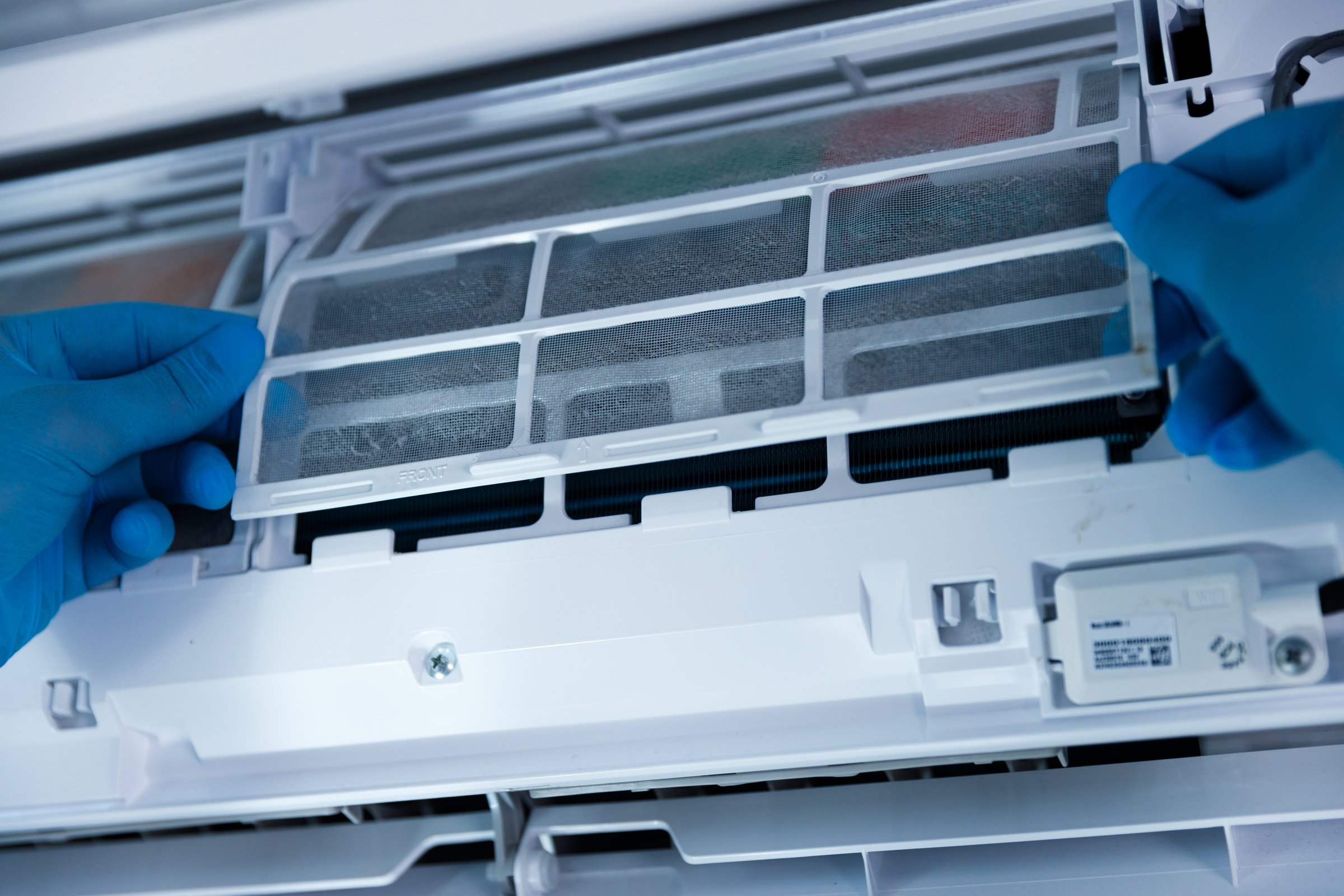 A close-up image features a person wearing blue gloves skillfully removing an air conditioner filter, emphasizing the importance of regular cleaning for health and functionality.
