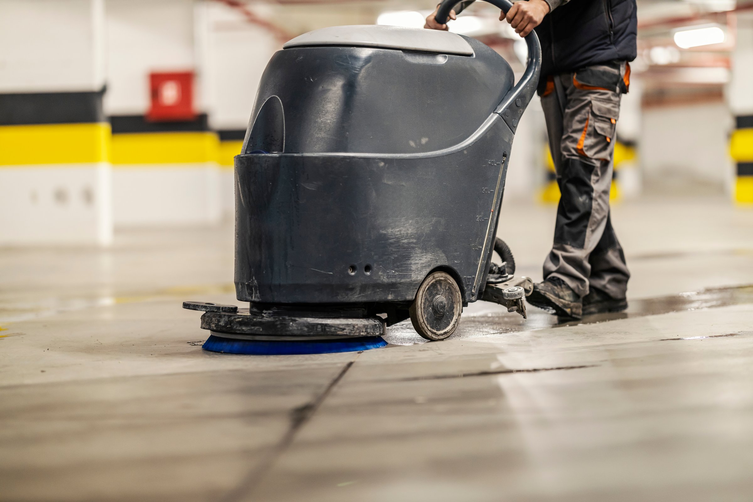 Cropped picture of unrecognizable worker washing garage floor with scrubber machine.
