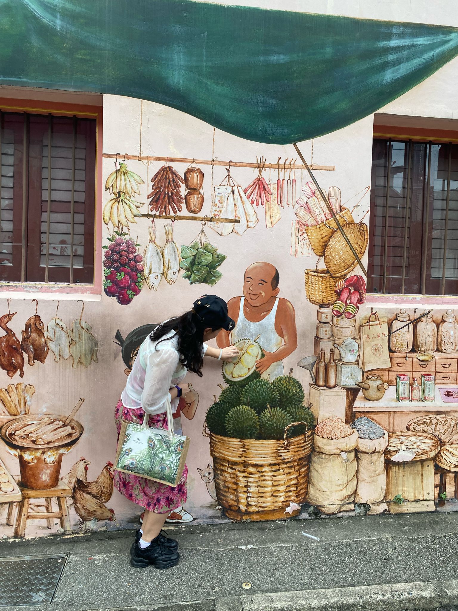 Person interacting with a mural of a street vendor selling various goods, including durians, hanging meats, and spices.