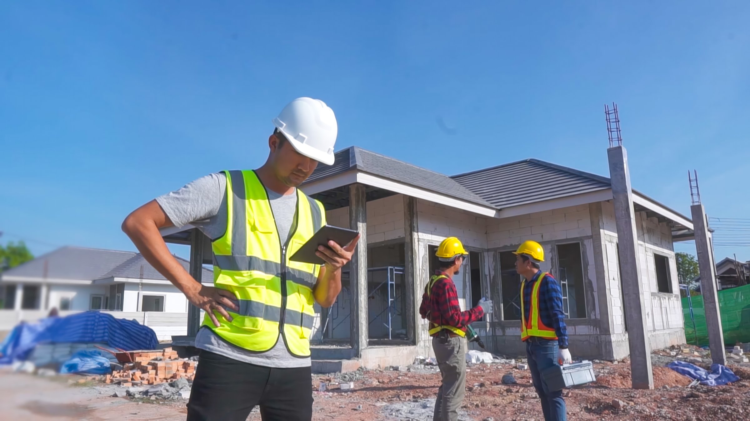 Engineer man using a tablet standing at a construction site Two construction workers in the background to explain home design work.