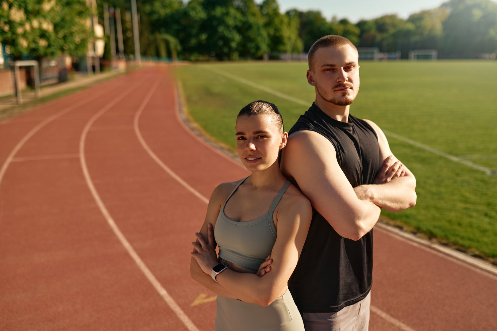 Strong athletic couple posing with crossed arms on a stadium track under the sun. Concept: teamwork, fitness motivation, health, discipline, power, mutual support, sports lifestyle.