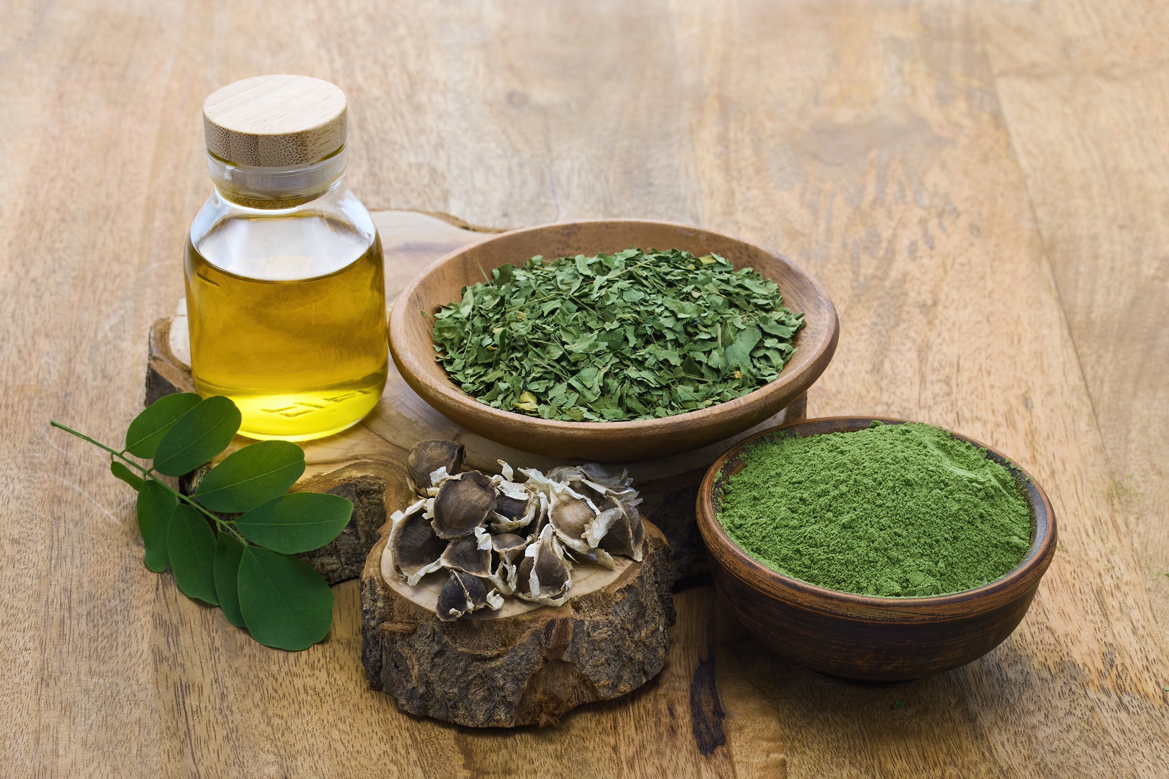 Moringa oil, leaves, seeds, and powder on a wooden surface.