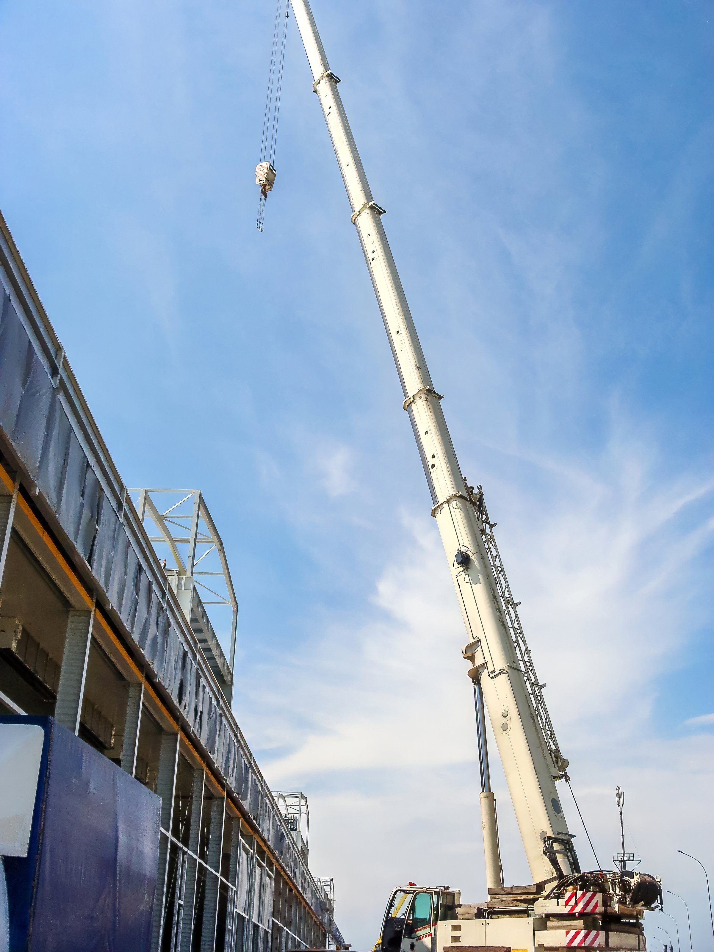 A telescopic mobile crane is seen on a construction site against a blue sky, aiding in the building's progress.