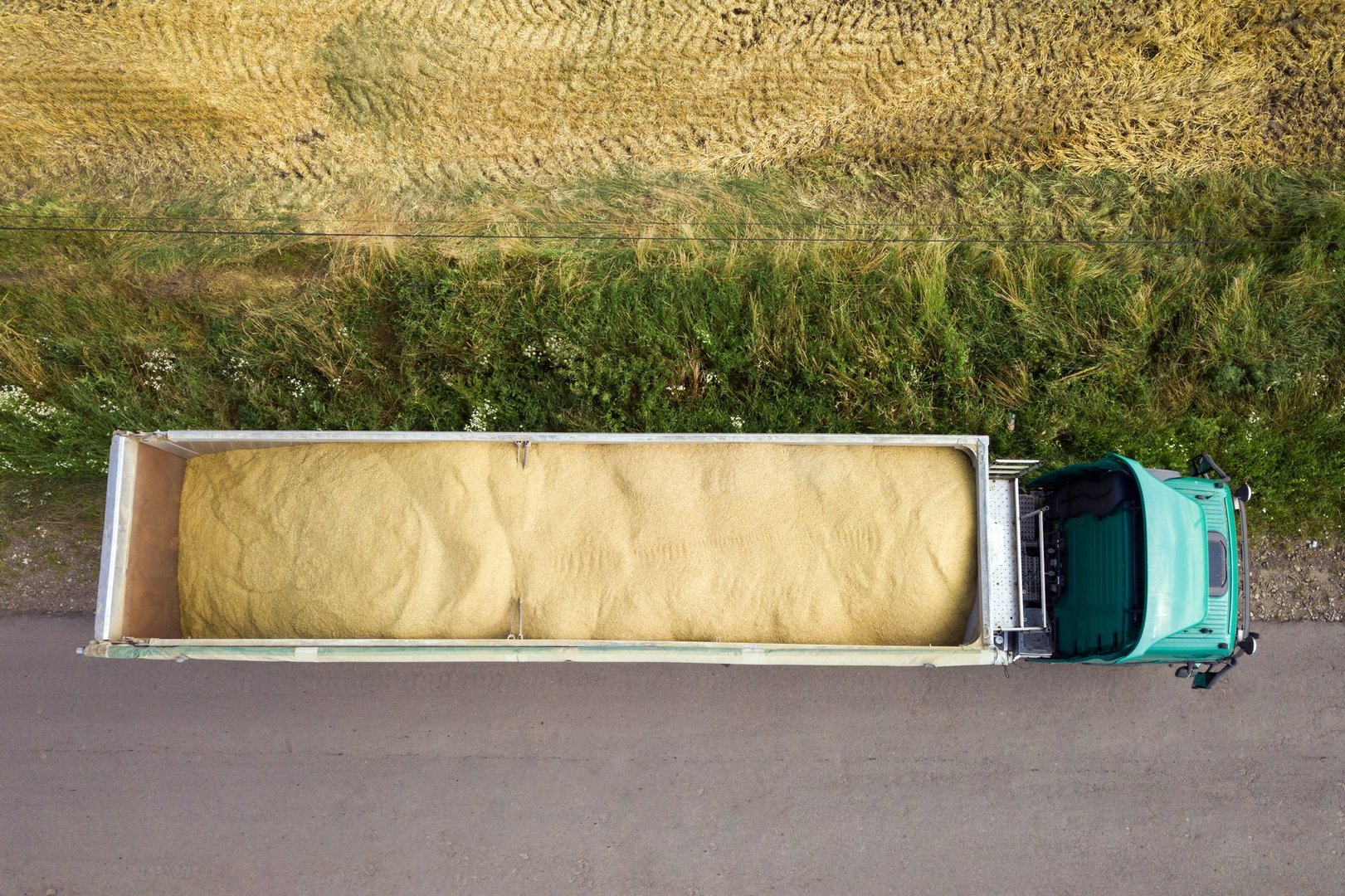 Aerial view of cargo truck driving on dirt road between agricultural wheat fields