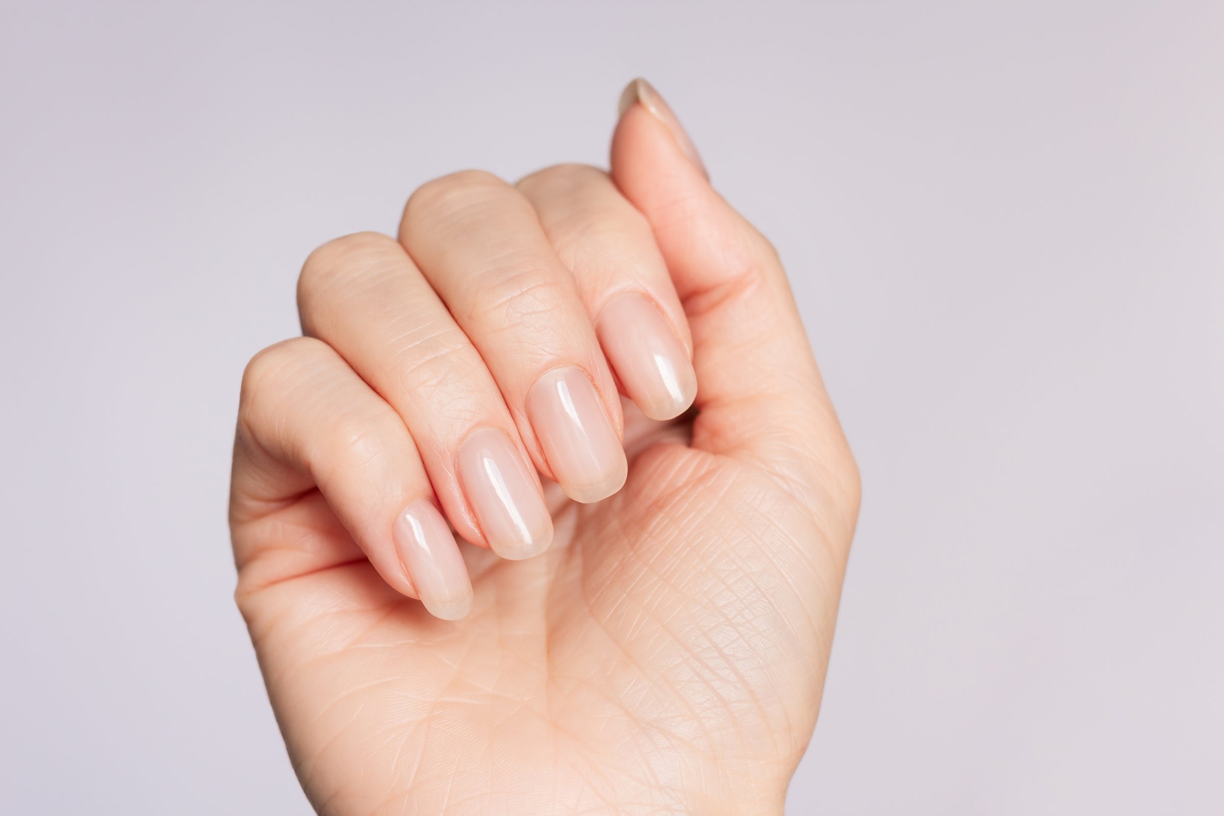 a close-up shot of a well-groomed female hand with a beautiful delicate fashionable nude manicure on a white background. Beauty and hand care
