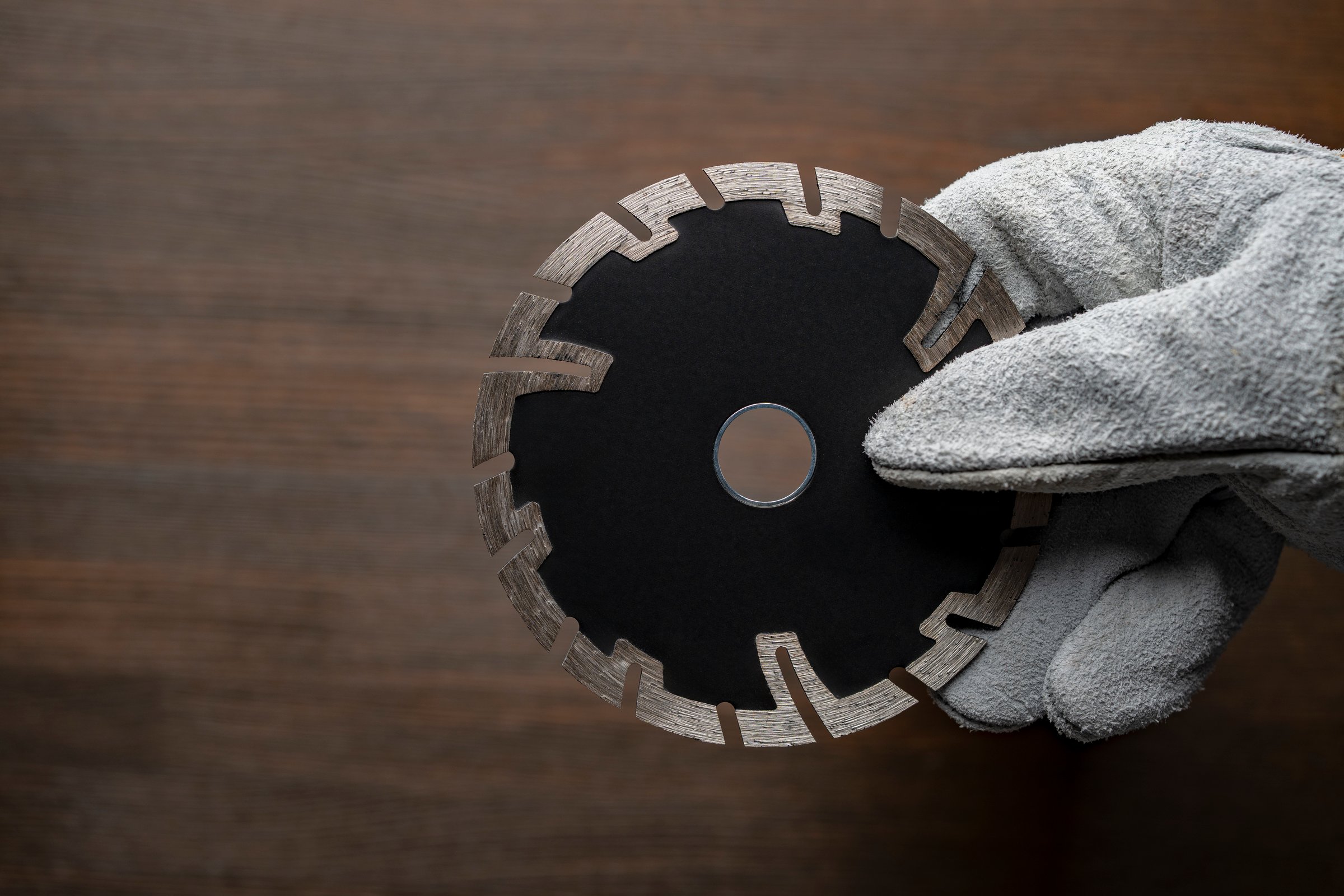 Worker hand in construction gloves holding new black diamond disc for cutting stone, concrete, brick and granite, close up, copy space
