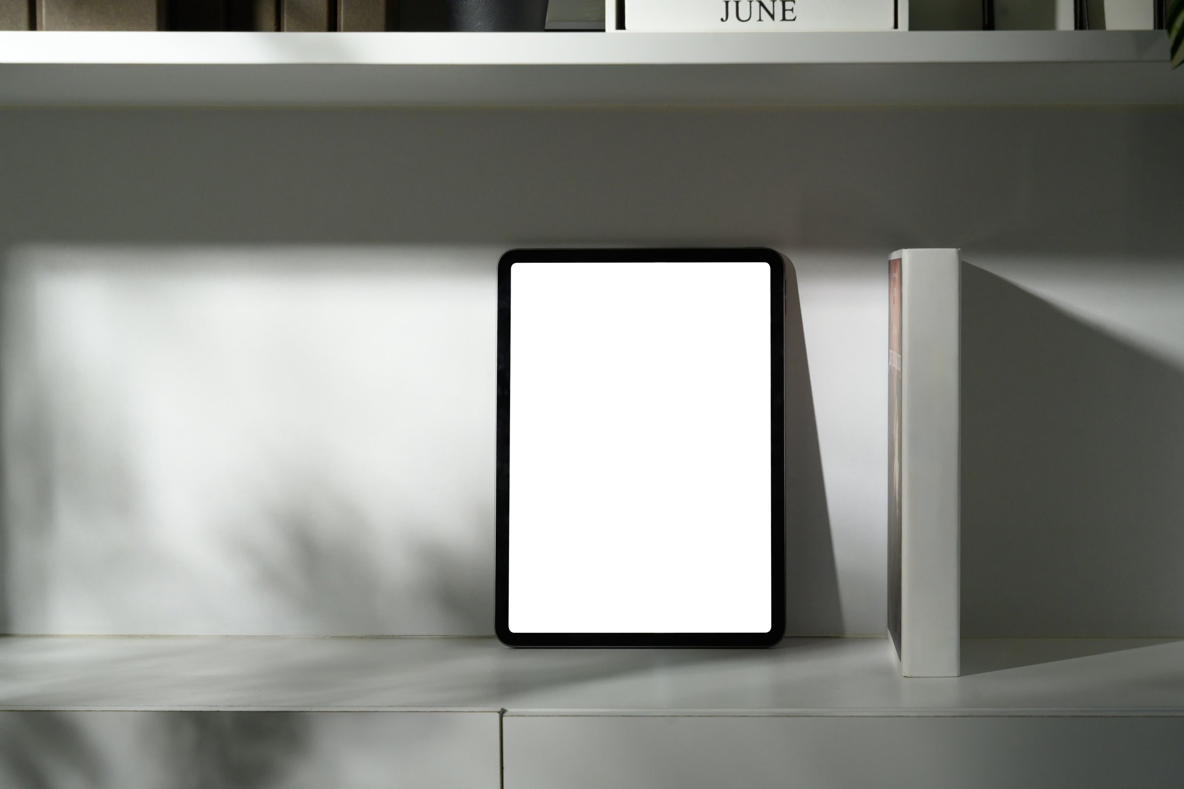 Digital tablet with empty screen propped upright on office shelf with soft shadows.