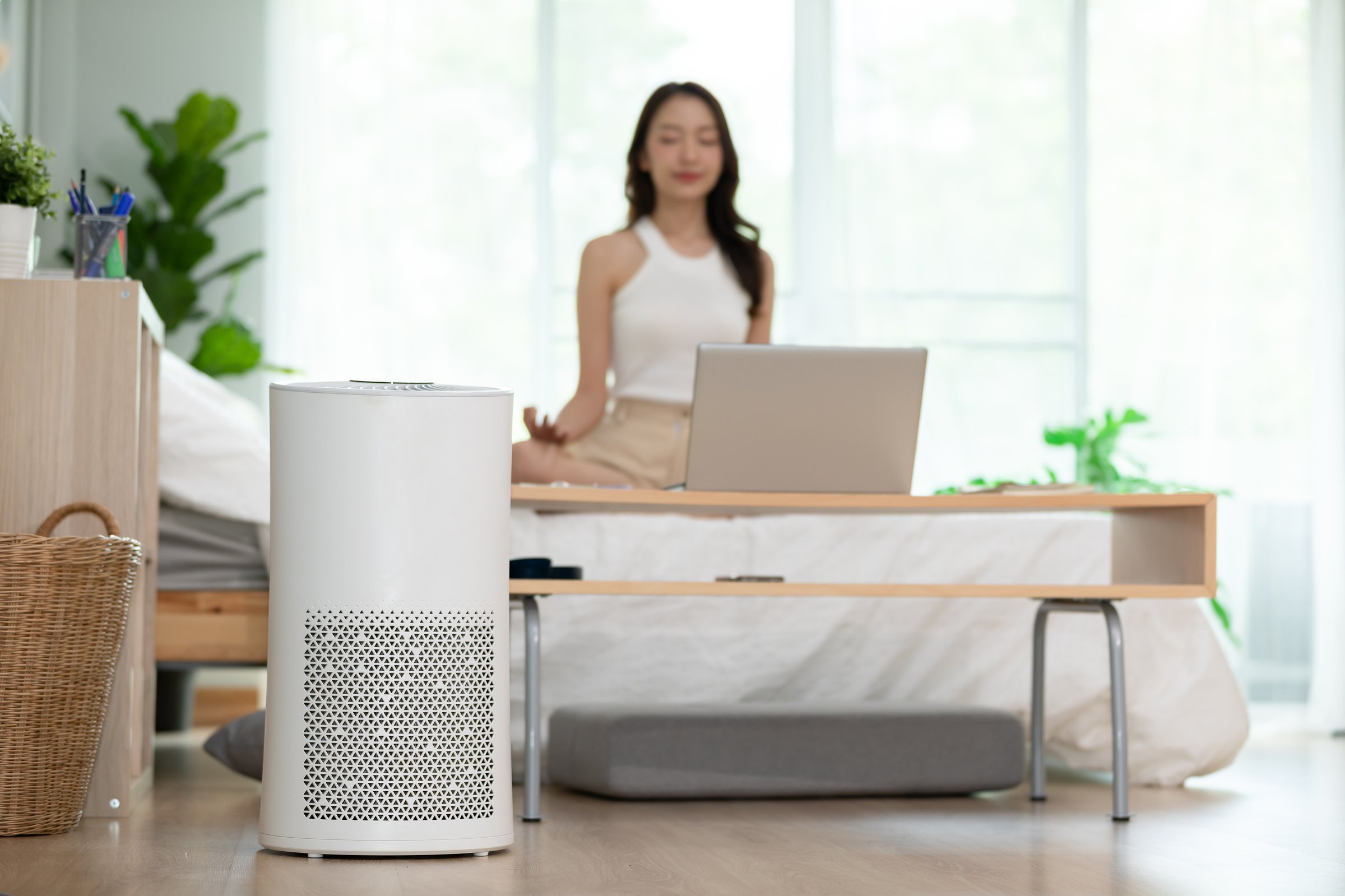 Air purifier in cozy white Living room for filter and cleaning removing dust PM2.5 HEPA at home with woman exercise yoga in background,for fresh air and healthy life,Air Pollution Concept