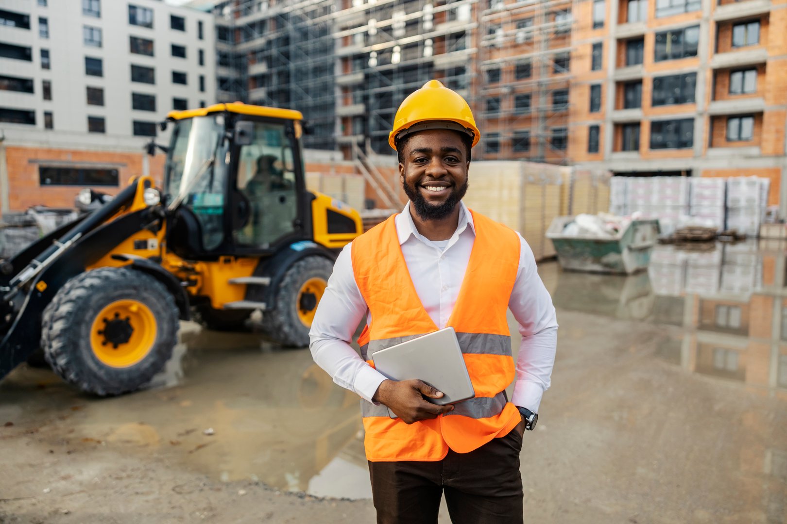 Portrait of african american engineer standing at construction site and smiling at camera.