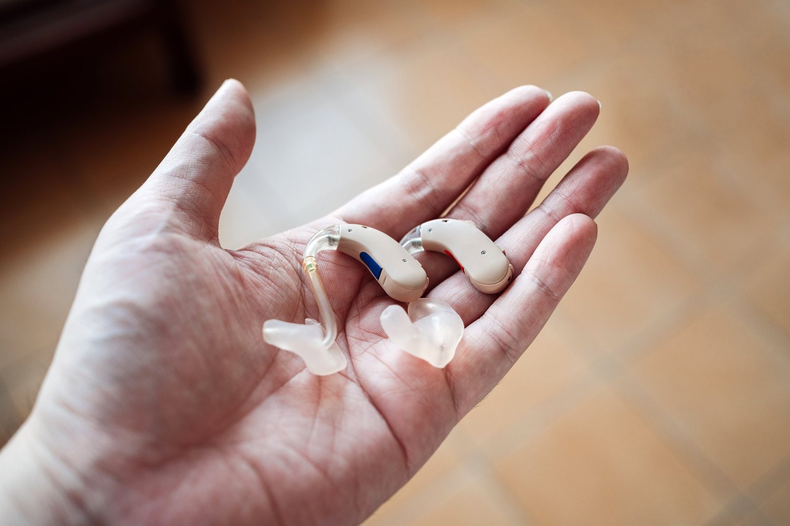 A hand holding a pair of modern hearing aids with custom ear molds, symbolizing accessibility, assistive technology, and healthcare innovation. Concept of hearing loss, support, and elderly care.