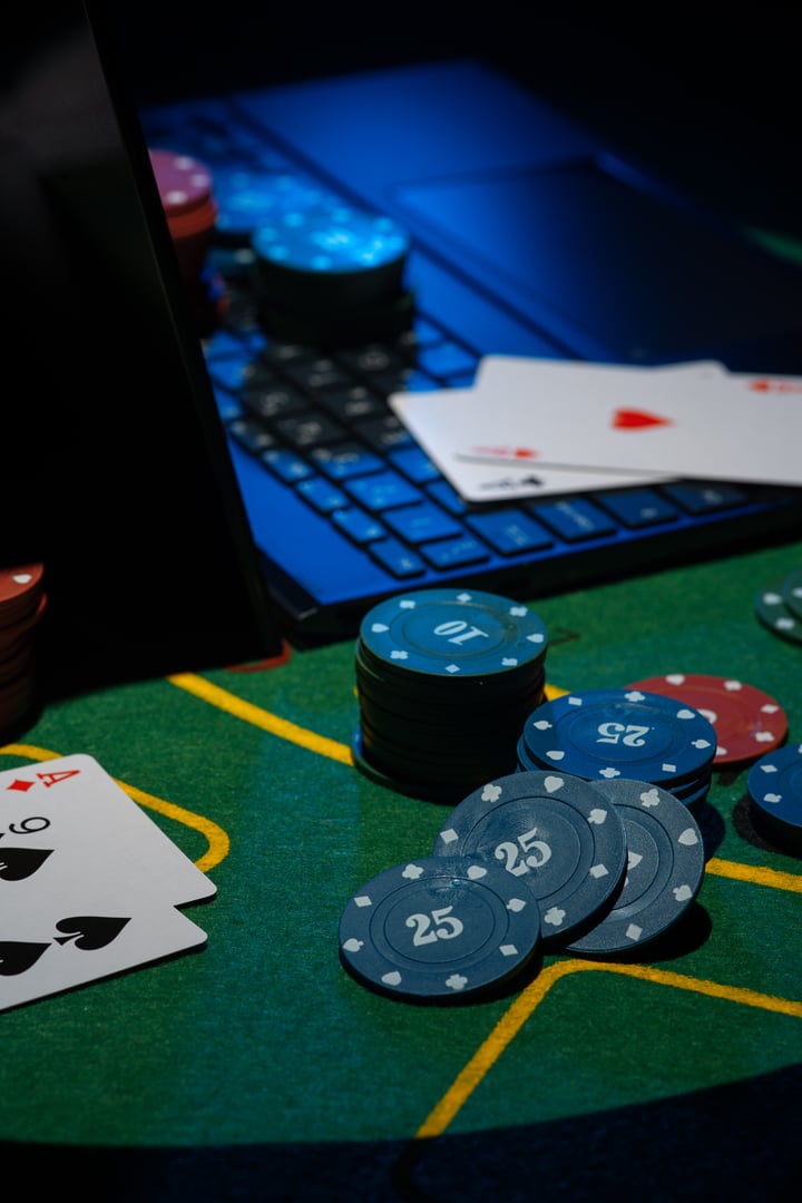 Scattered poker chips and cards on a green table with and laptop