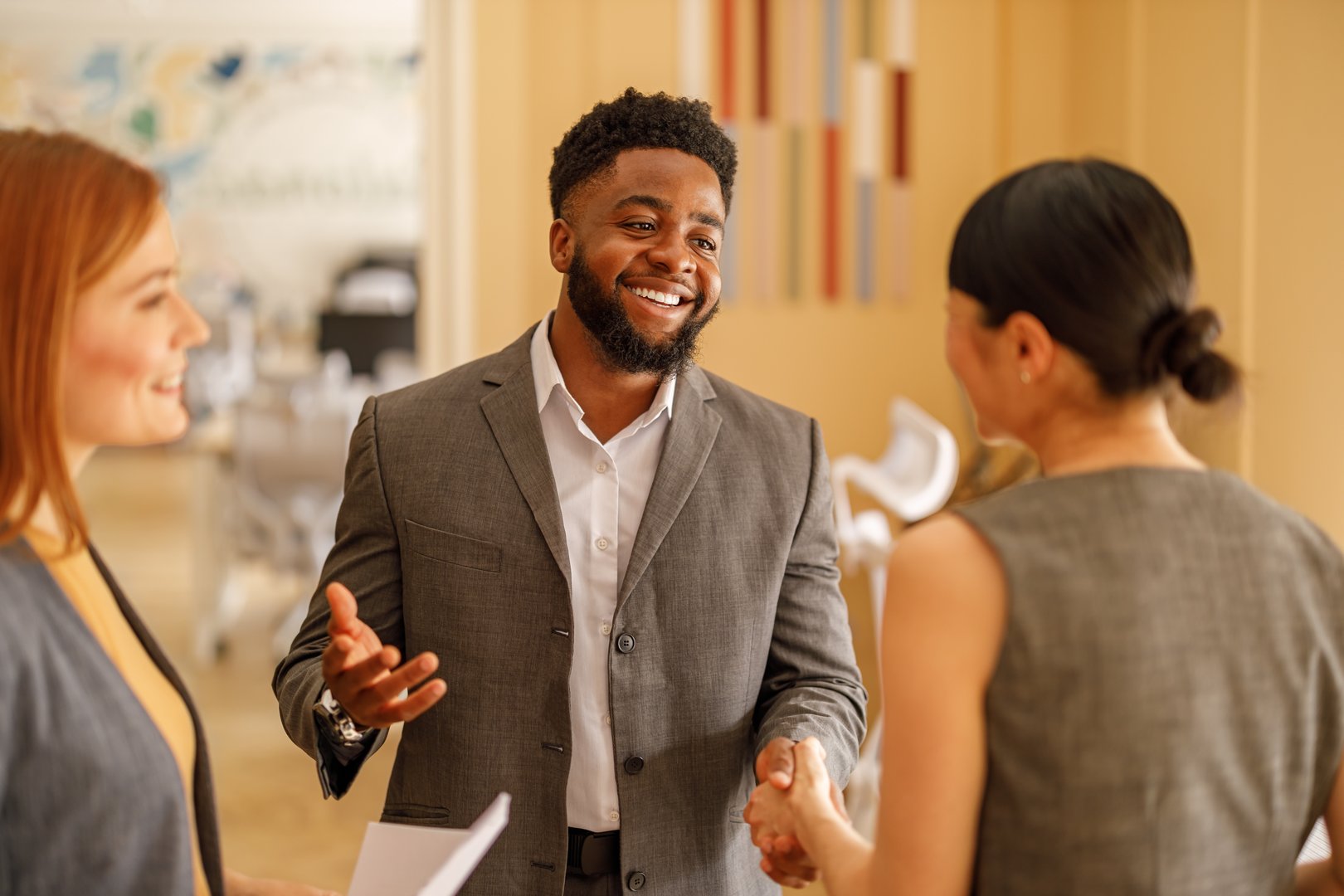 Smiling businessman greeting female colleagues with handshake at start of corporate strategy meeting