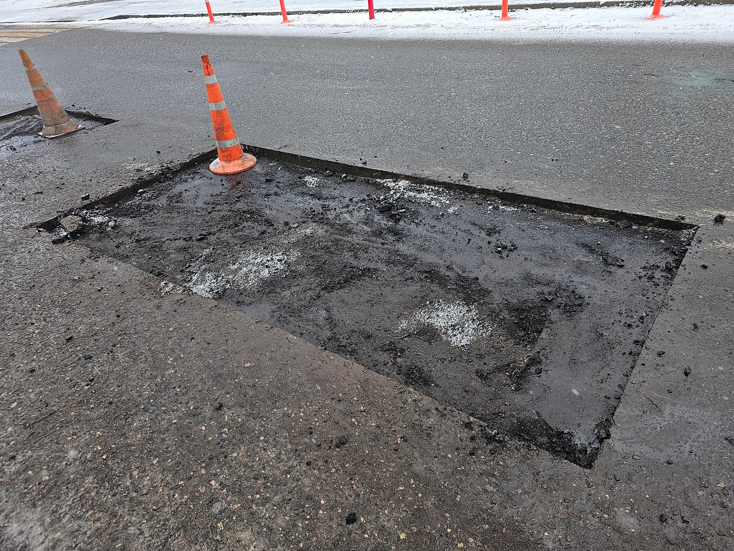 Pothole repair efforts underway on busy road with construction cones marking hazardous area