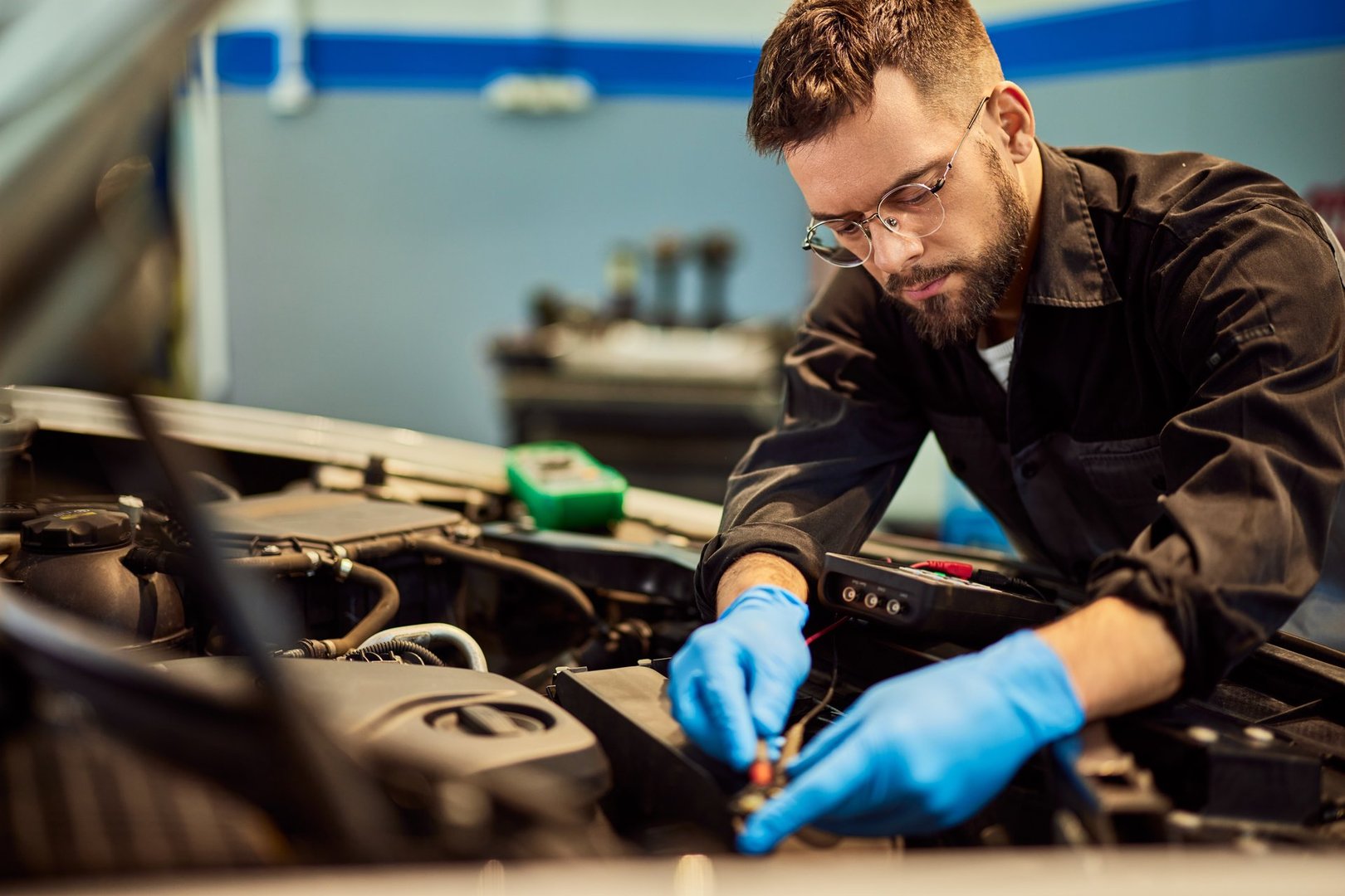 A man works as a mechanic, fixing a car, and connecting some cables