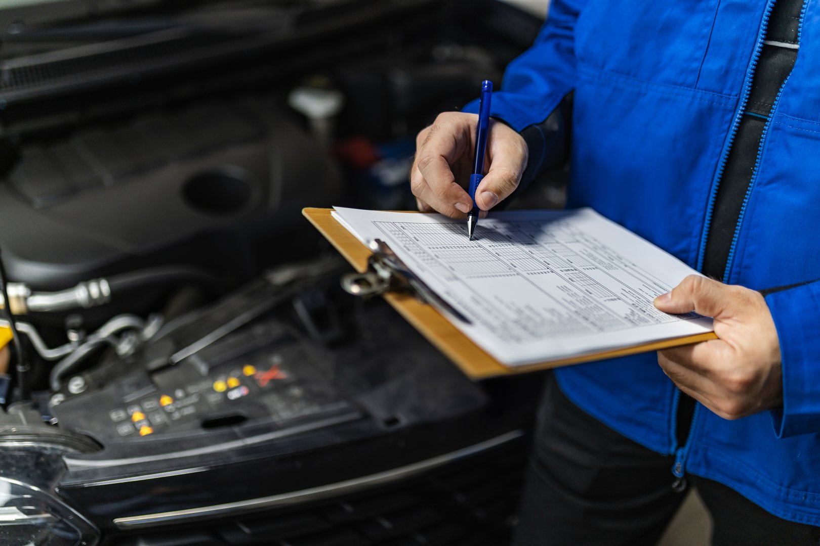A skilled mechanic reviews a detailed maintenance checklist while inspecting the engine of a car in a well-equipped workshop, ensuring proper functionality and safety.