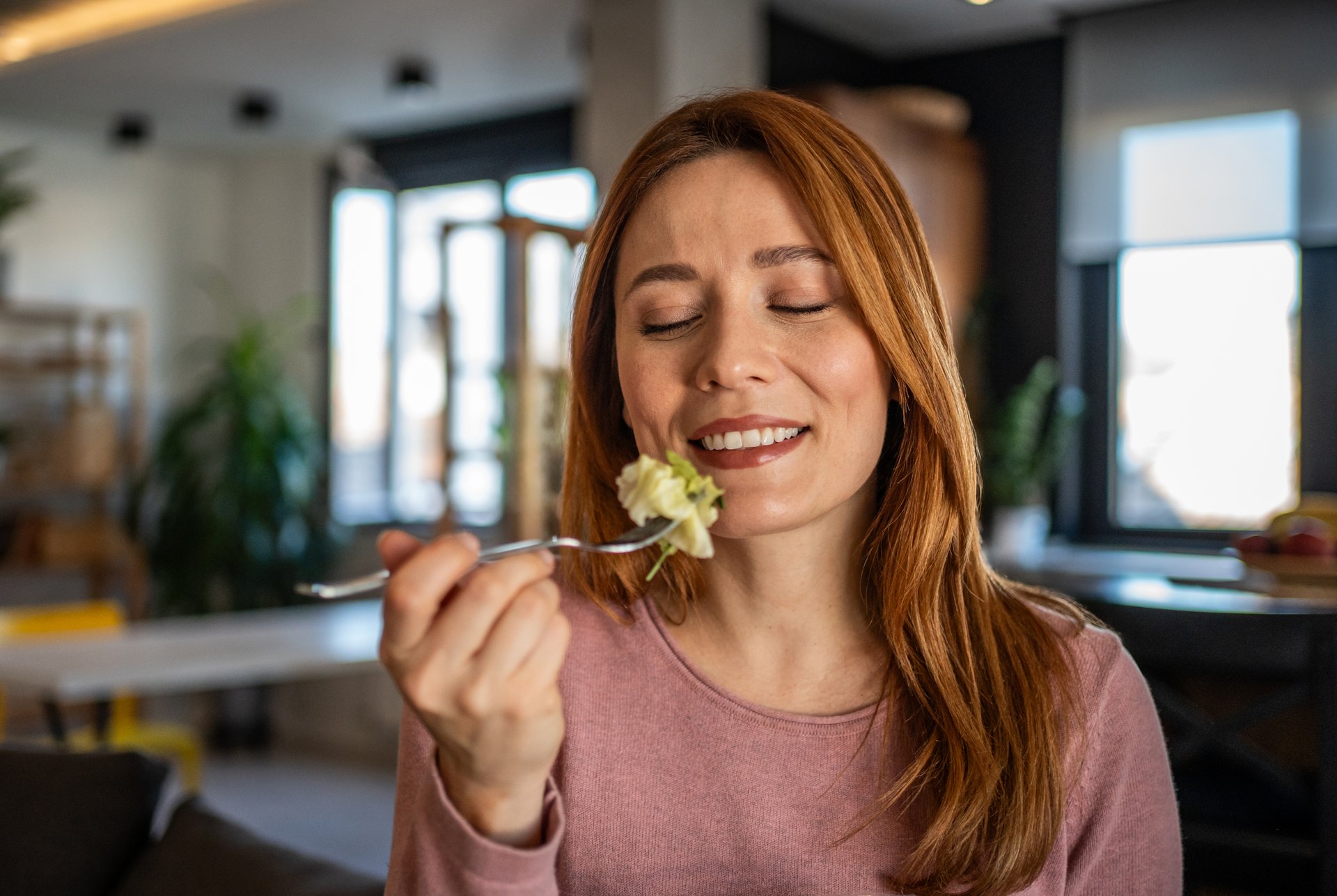 Smiling redhead woman savoring a bite of fresh salad, enjoying a nutritious meal in the comfort of a modern kitchen, embracing a healthy lifestyle and the pleasure of mindful eating