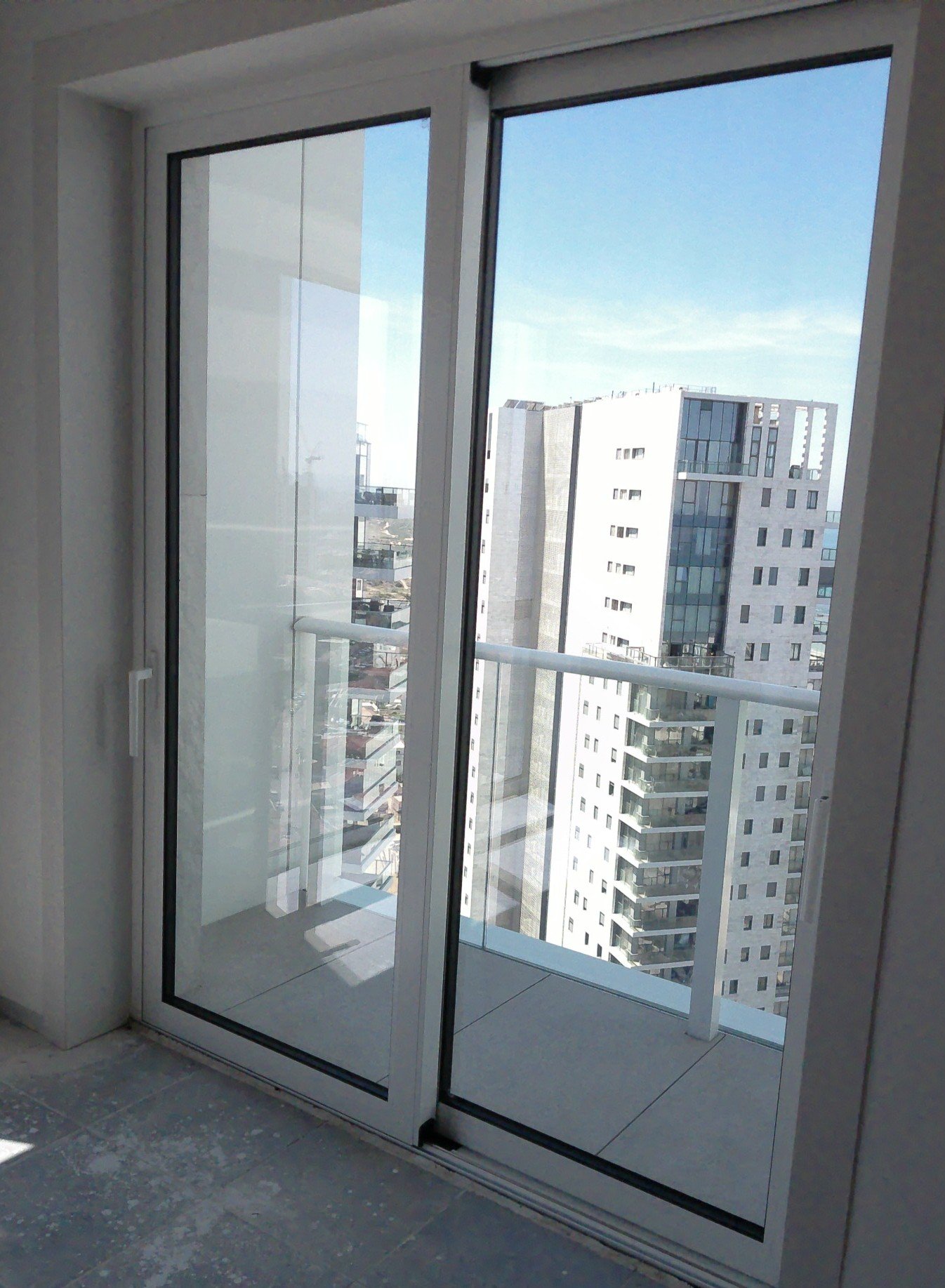 Glass balcony doors with a view of modern high-rise buildings and a clear blue sky.