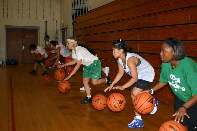 A group of people practicing basketball dribbling drills in a gym. Theyre lined up, each bouncing a basketball.