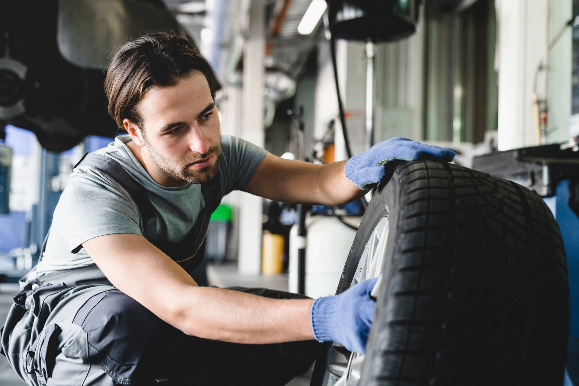 MOT. Vehicle inspection. Caucasian male young car technician mechanic repairing fixing wheel tire of automobile at service station