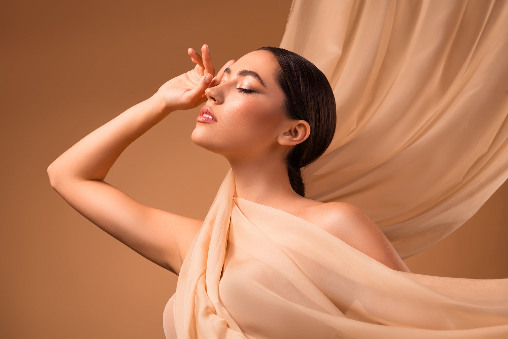 Graceful depiction of a young brunette woman posing elegantly against a beige backdrop, emanating beauty, sophistication, and serene confidence.