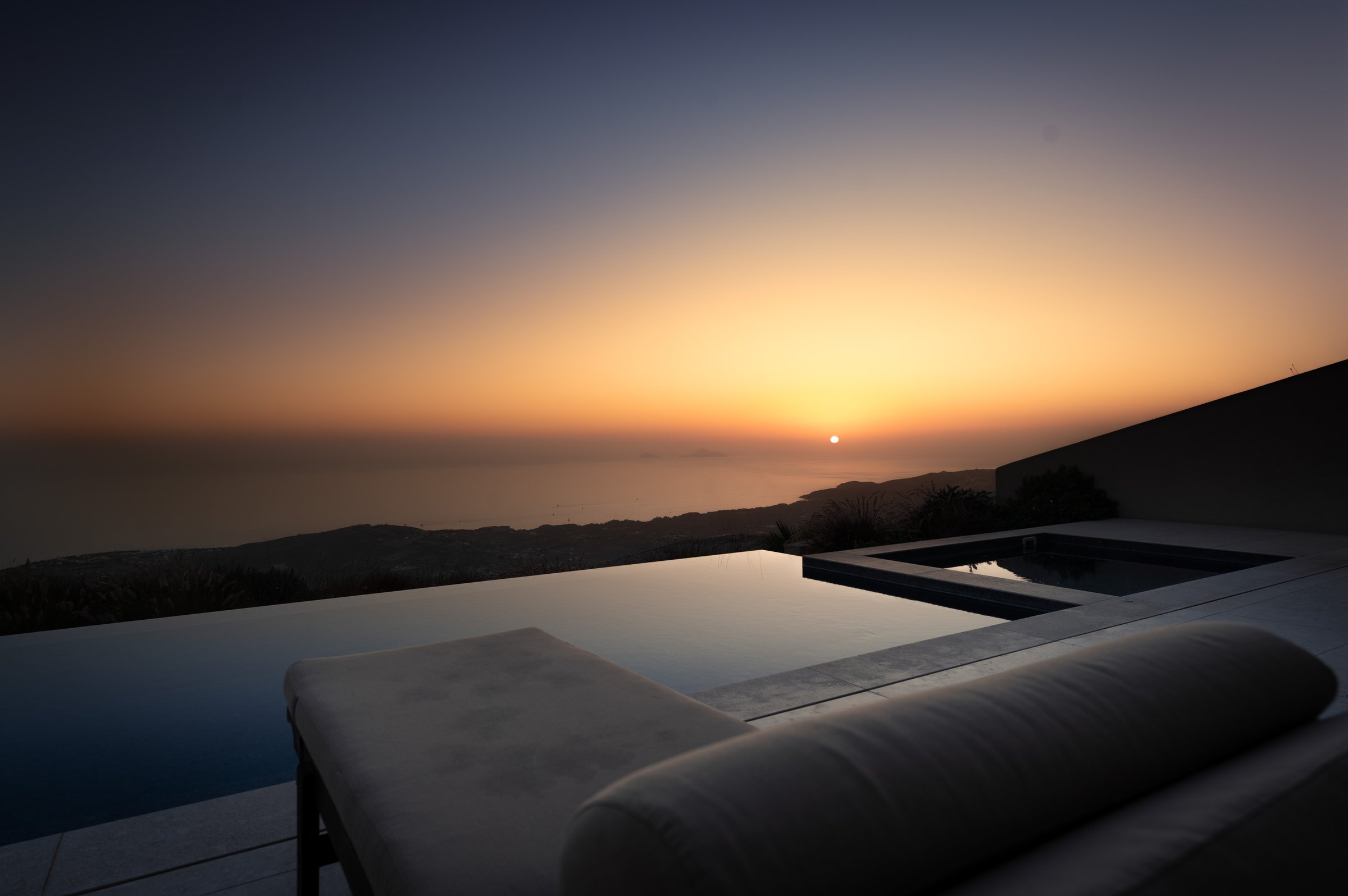 The sun dips below the horizon, casting a warm glow over a tranquil pool that overlooks the vast expanse of the ocean.
